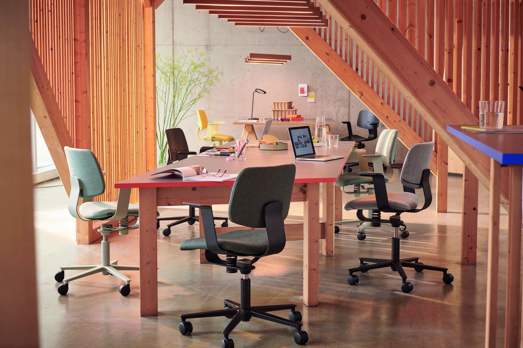 Mehrere Wilkhahn 228 WiChair Bürostühle in verschiedenen Farben um einen Holztisch in einem modernen Büro.