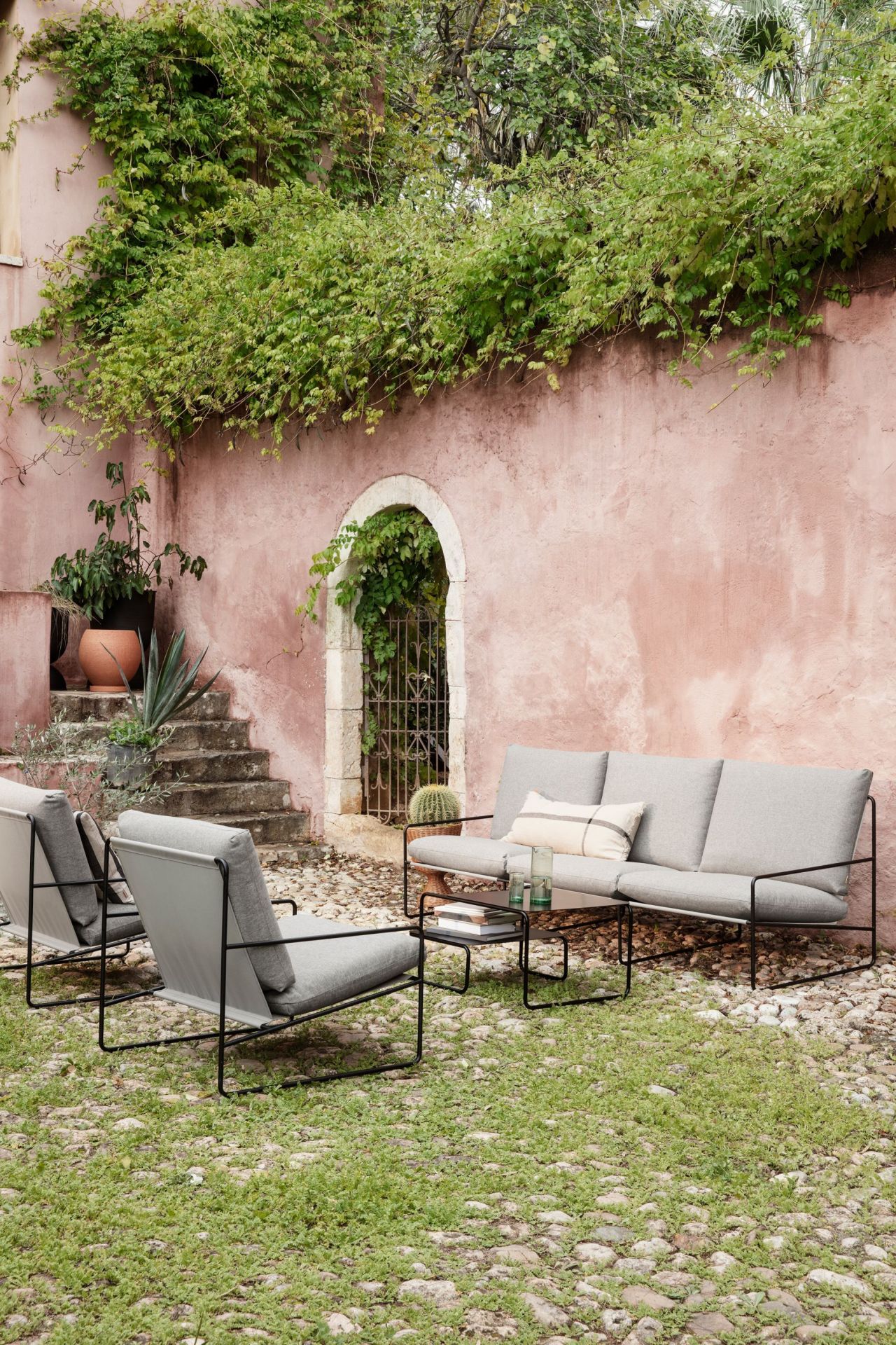 Ferm Living Desert Sessel mit schwarzem Gestell und grauer Sitzfläche im Garten mit Outdoor-Möbeln.