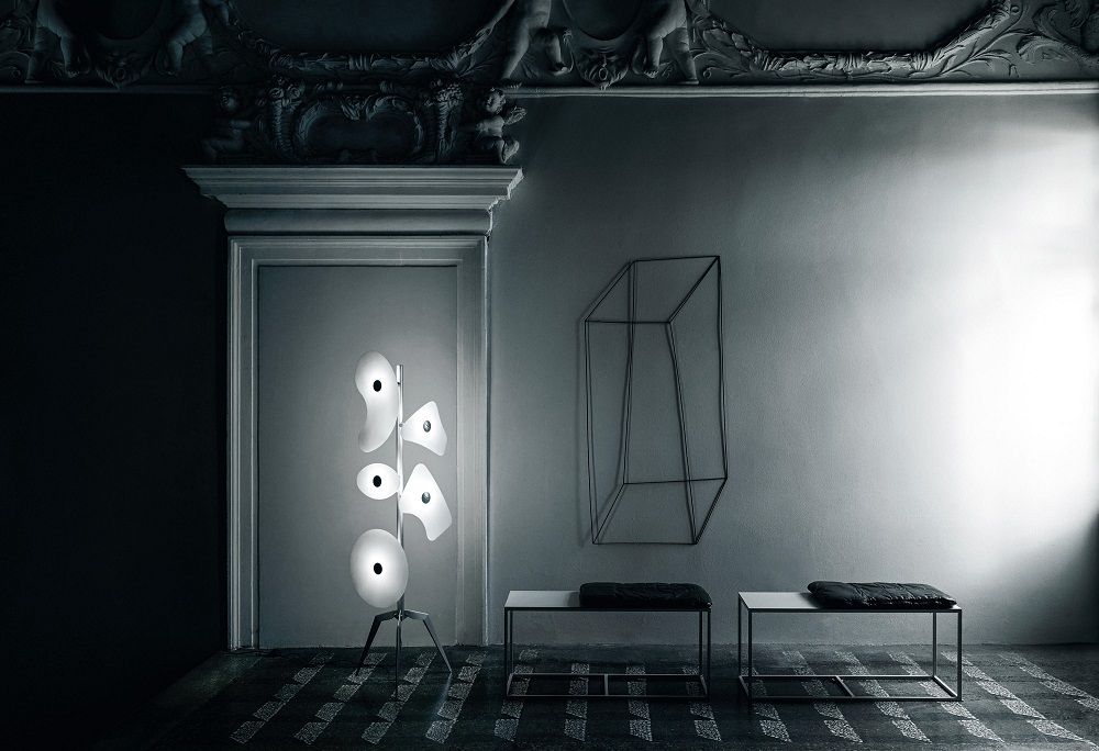Moderne Stehlampe mit fünf Leuchten in Weiß, minimalistische Bänke und Drahtkunst an grauer Wand.