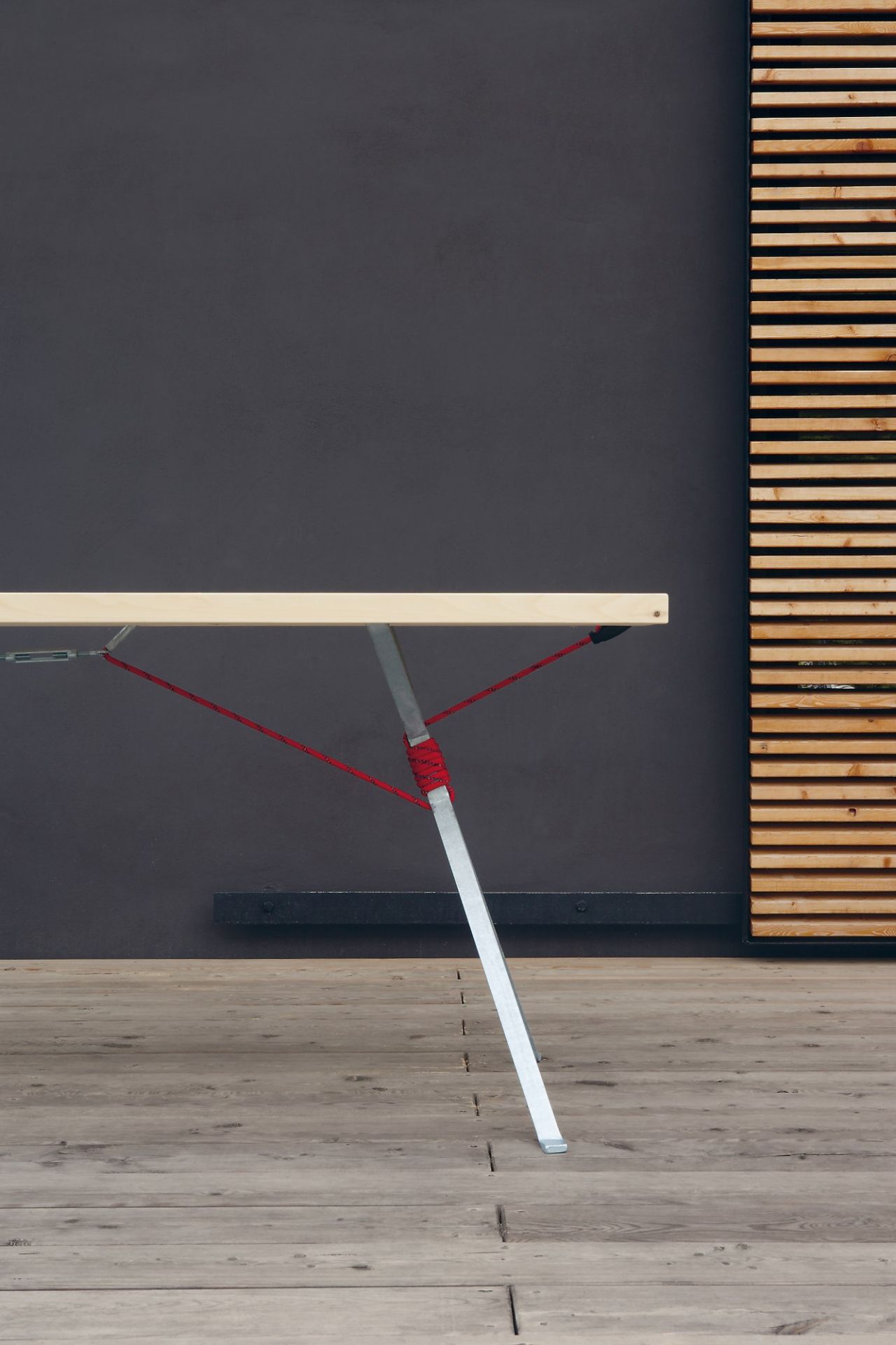 Detailaufnahme der Kampenwand Bank von Nils Holger Moormann, minimalistisches Design mit roter Seilkonstruktion und Holzplatte.