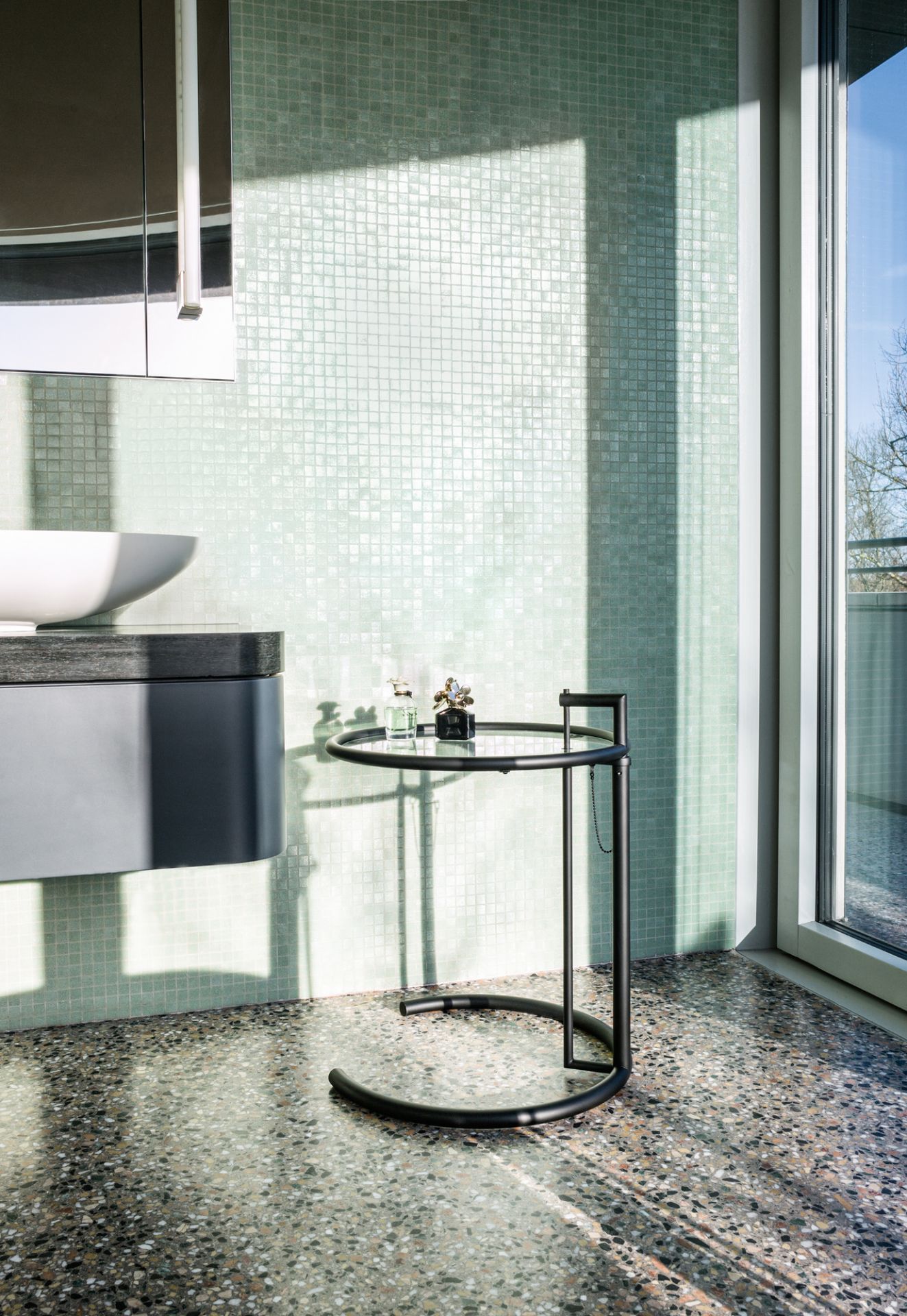 ClassiCon E1027 Beistelltisch, höhenverstellbar, mit Glasplatte und schwarzem Gestell im modernen Badezimmer.
