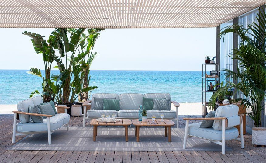 Emu Twins Sofa Outdoor-Lounge-Set auf Holzterrasse mit Meerblick, bestehend aus Sofa, Sessel und Couchtischen.