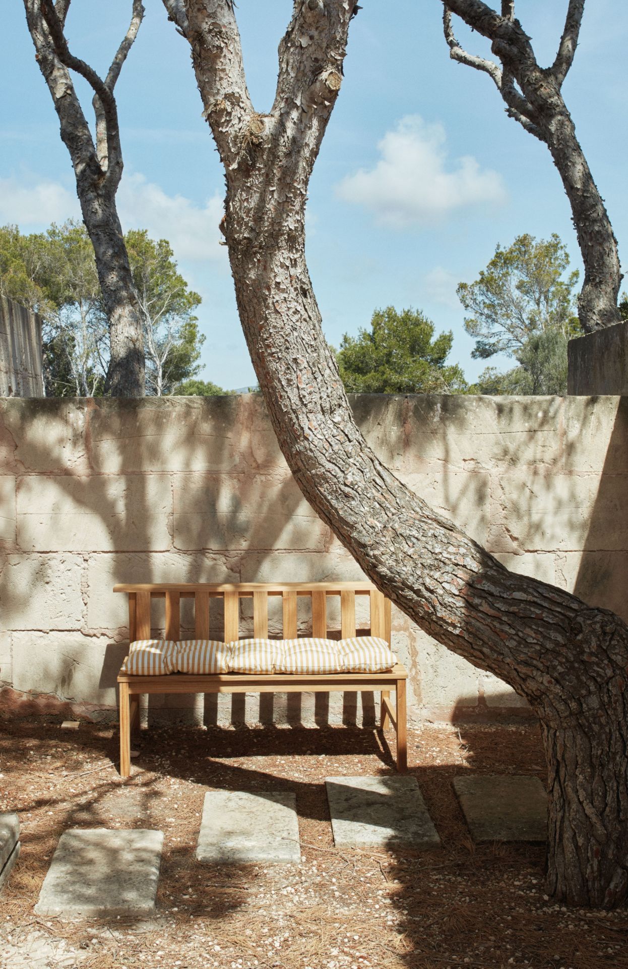 Cadence Bank Teakholz Gartenbank von Skagerak by Fritz Hansen mit gestreiften Kissen unter Baum.