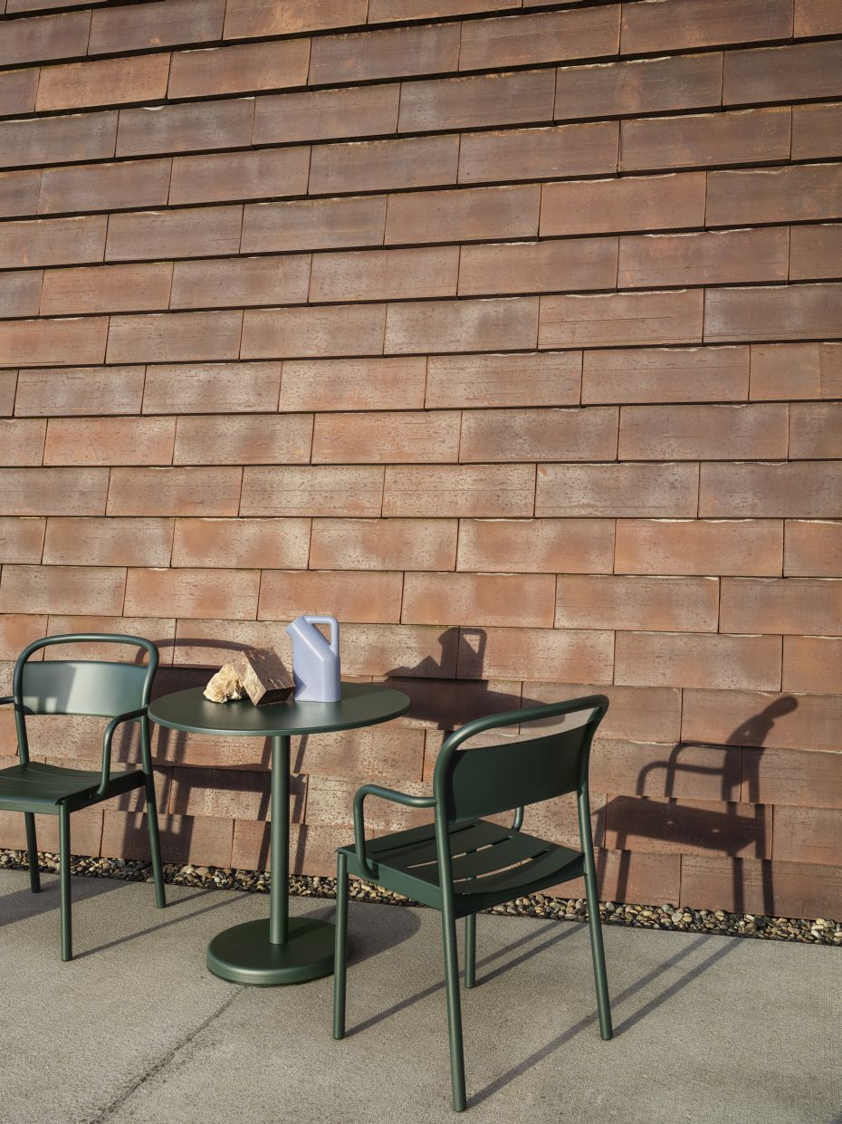 Grüner Muuto Linear Steel Outdoor Beistelltisch mit zwei Stühlen und Dekoration vor Ziegelwand.