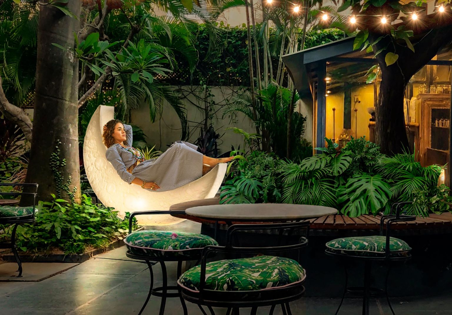 Frau entspannt in der leuchtenden My Moon Lampe von Seletti im Gartenambiente mit tropischen Pflanzen.