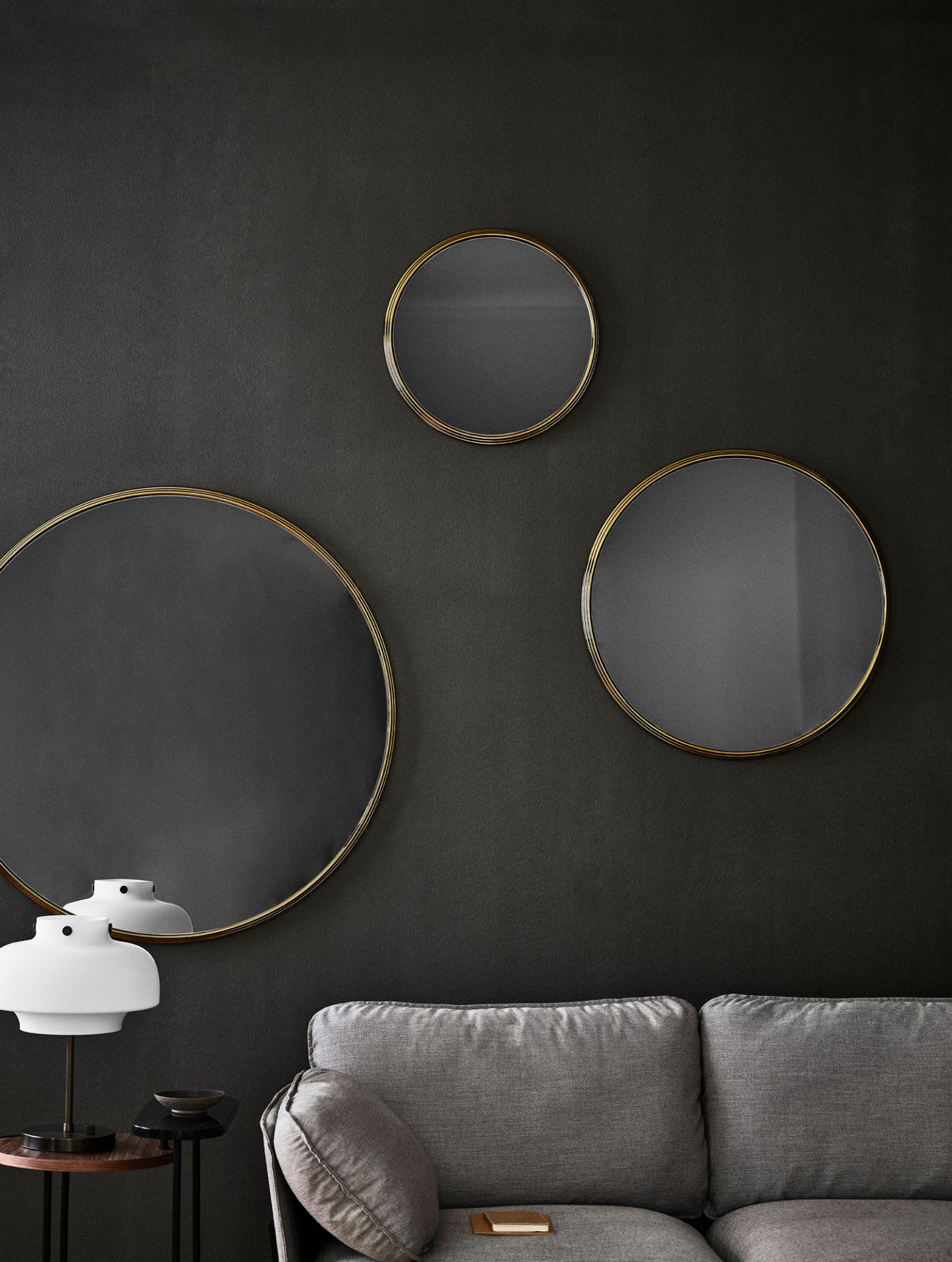 Graues Cloud 2-Sitzer Sofa von AndTradition mit runden Spiegeln und Lampe vor dunkler Wand.