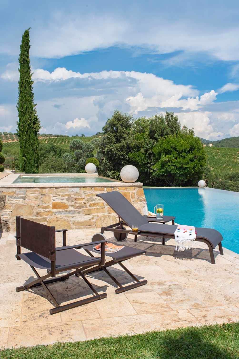 Terra Fußhocker von Emu neben Liegestuhl am Pool, ideal für entspannte Stunden im Freien.