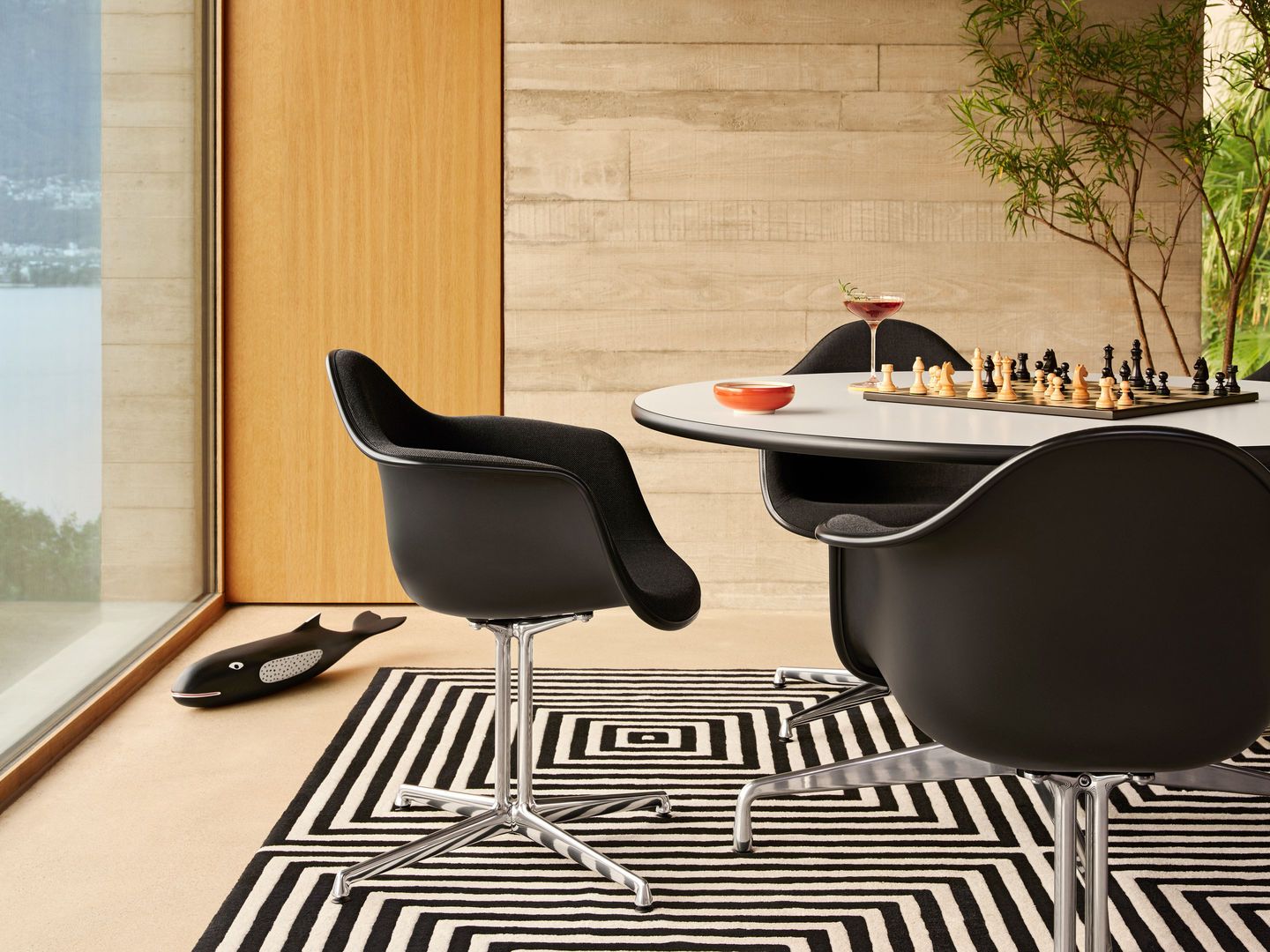 Schwarzer Eames Plastic Arm Chair DAL mit Sitzpolster von Vitra am Esstisch mit Schachbrett.