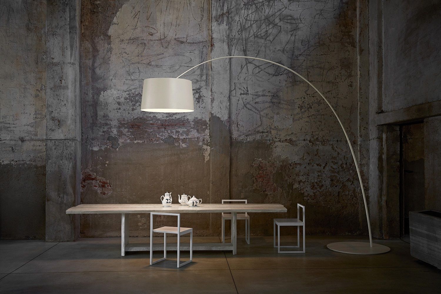 Weiße Twiggy Bogenleuchte von Foscarini über Esstisch mit Geschirr in loftartigem Ambiente.