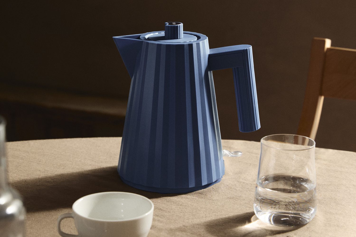 Blauer Alessi Plissé Wasserkocher mit Rillenstruktur auf einem Tisch, neben Tasse und Glas.