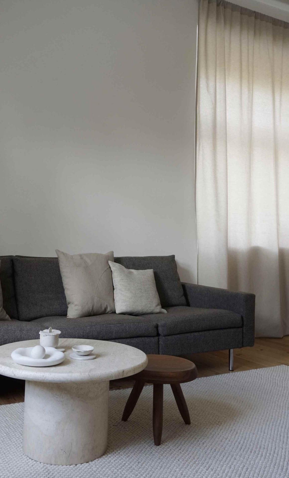 Wohnzimmer mit grauem Sofa und hellem Tact Rug Teppich von Woud, Größe 200x300 cm.