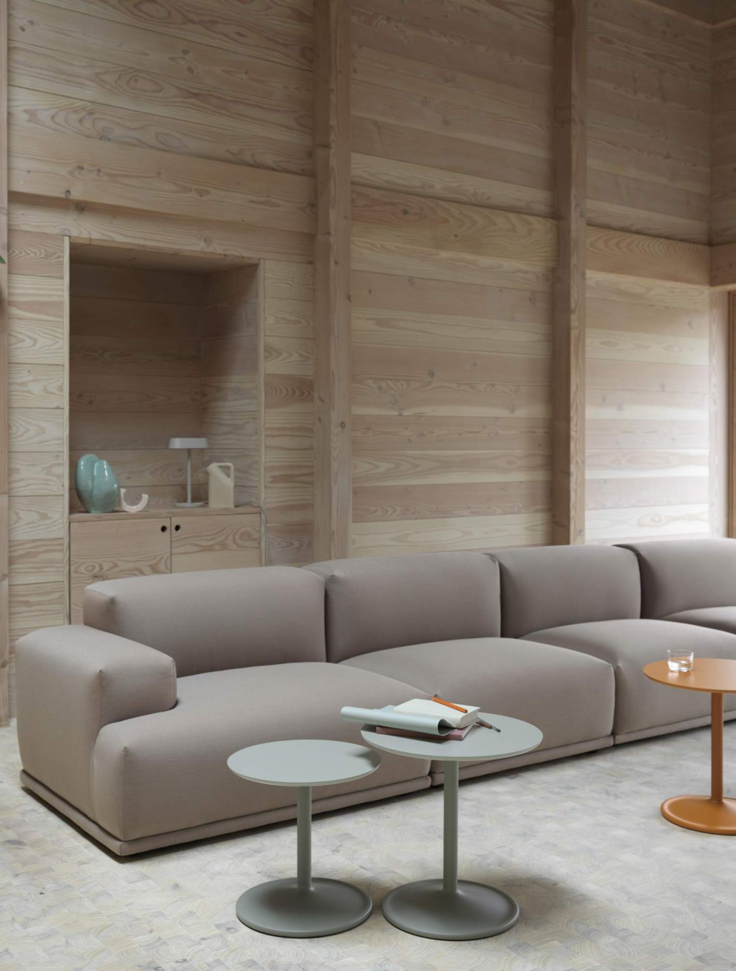 Muuto Soft Side Table Beistelltisch in Grau vor beigem Sofa und Holzwand, modernes Wohnzimmer Design.