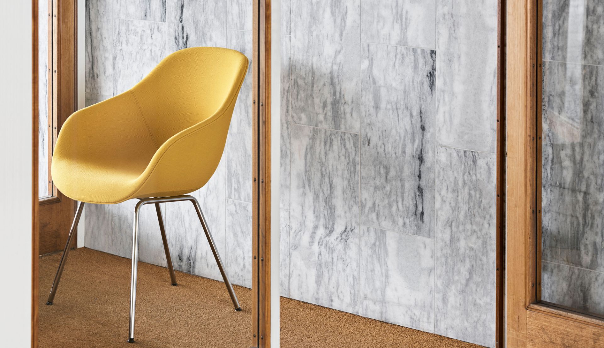 Gelber About a Chair AAC127 Stuhl von Hay mit verchromten Beinen vor Marmorwand.