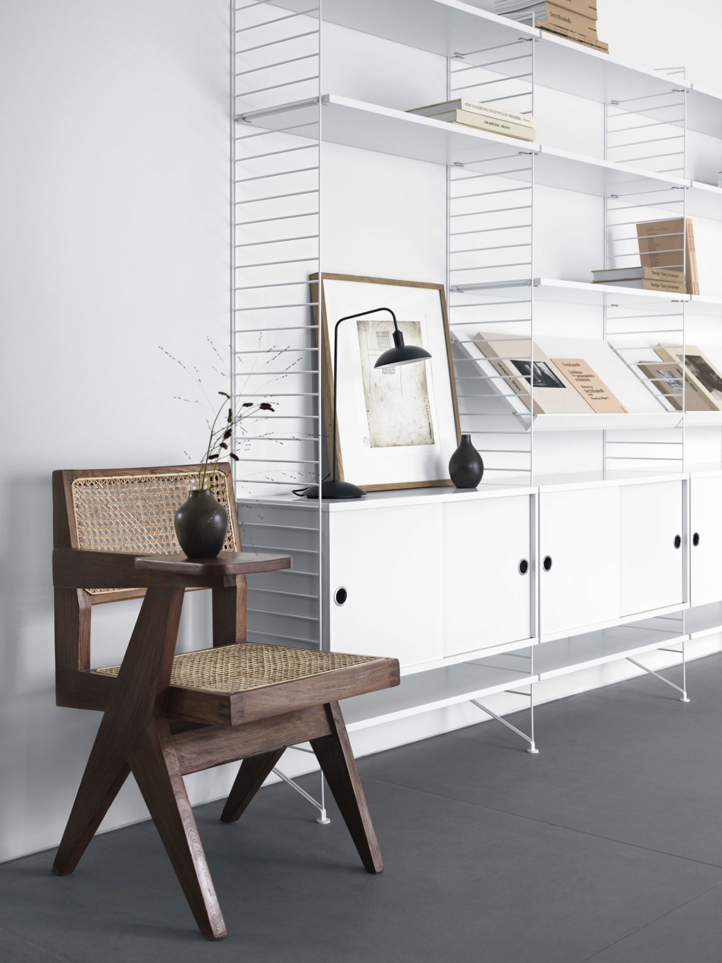 String Furniture Regalsystem mit Schrankelement und Schiebetüren in Walnuss, kombiniert mit Stuhl.
