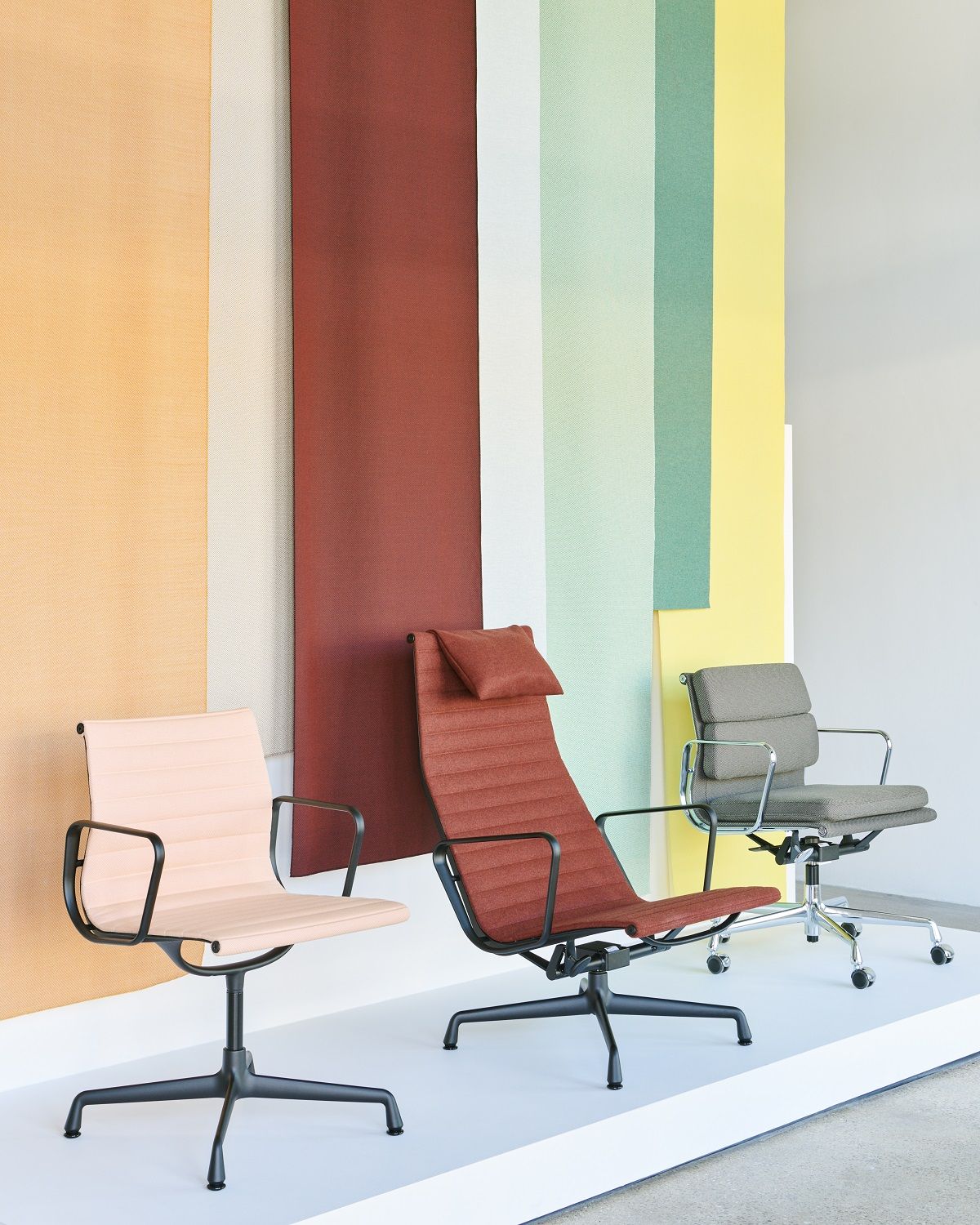 Drei Vitra Soft Pad Chairs EA217 in Beige, Rot und Grau vor farbigem Hintergrund.