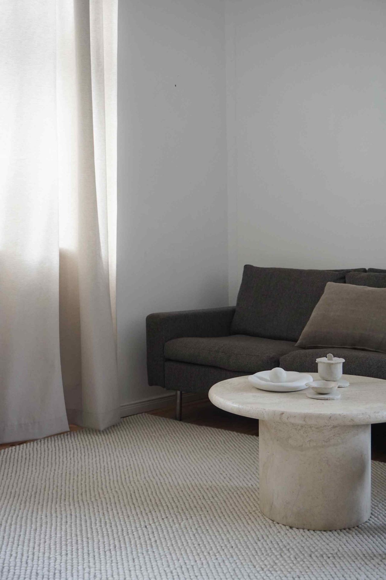Off-white Tact Rug Teppich von Woud, 170x240 cm, in einem minimalistischen Wohnzimmer mit Sofa.