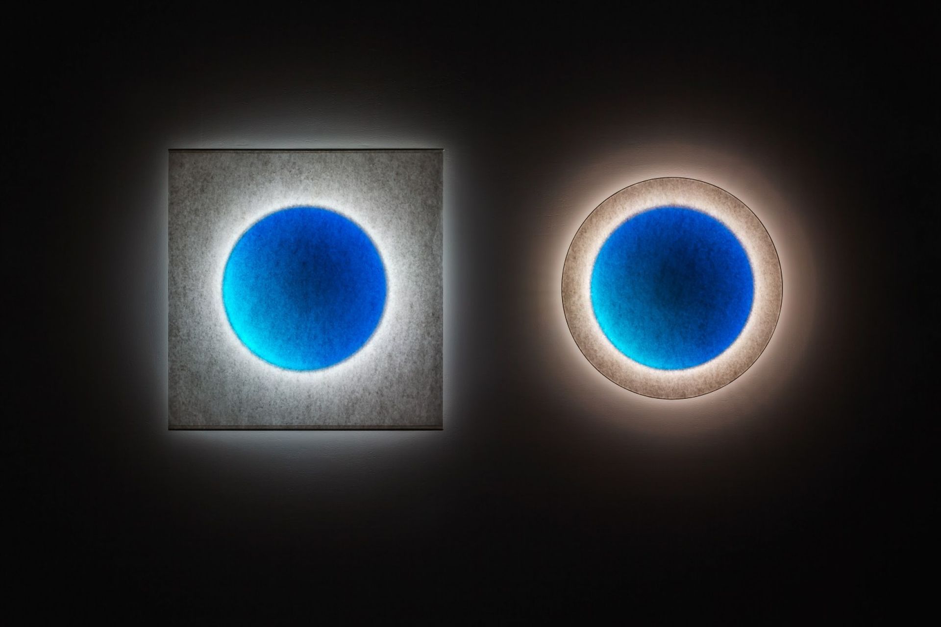 Zwei Moodmoon Wandleuchten: Rund und quadratisch, blaues Zentrum, indirekte Beleuchtung.