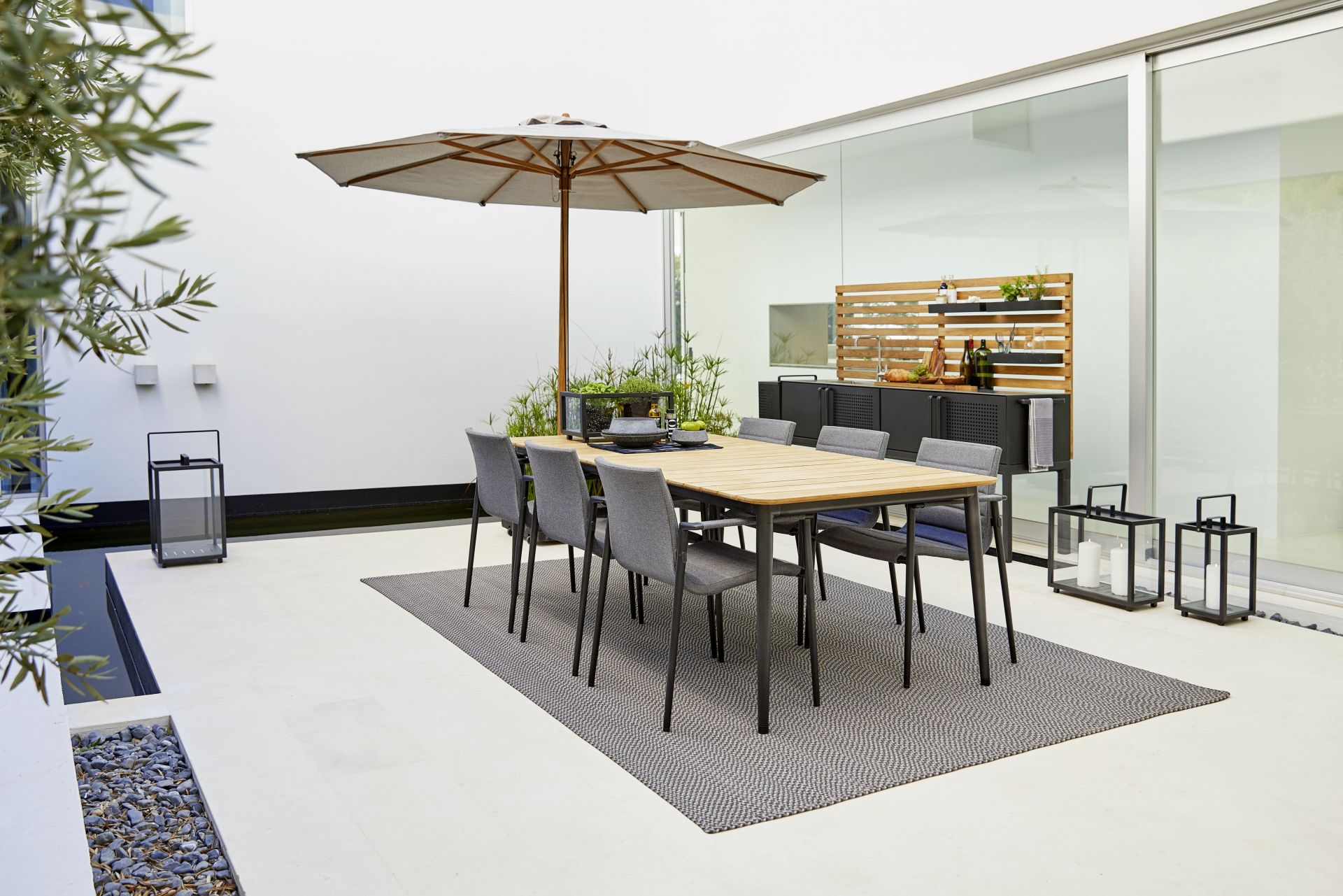 Gartenszene mit Cane-Line Sonnenschirm, Esstisch und Stühlen für stilvolle Outdoor-Gestaltung und Sonnenschutz.