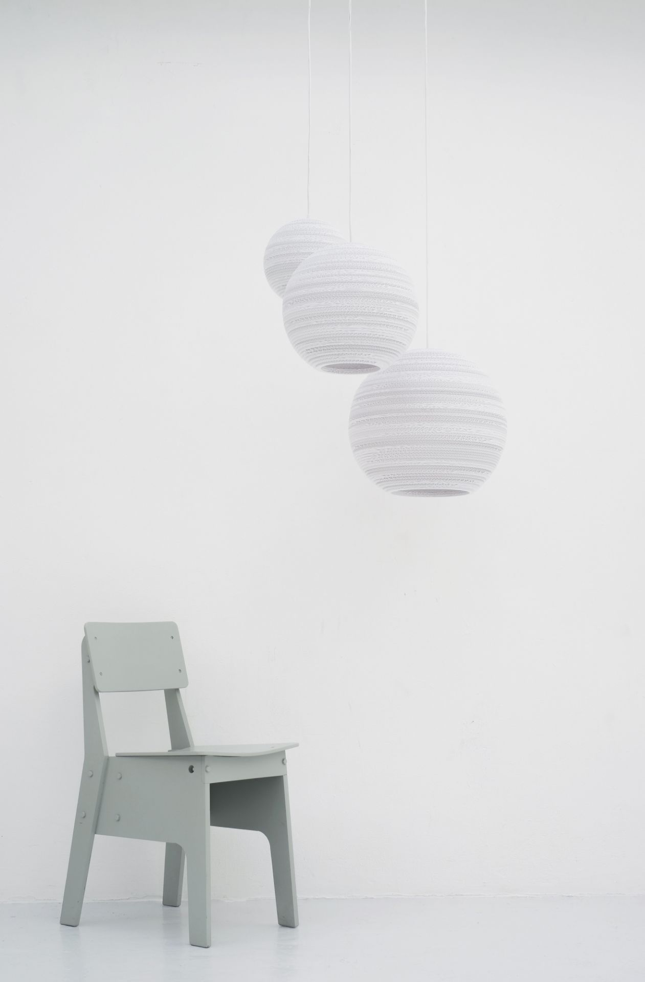 Drei Scraplights Moon Hängeleuchten von Graypants in Weiß über einem grauen Holzstuhl vor weißer Wand.