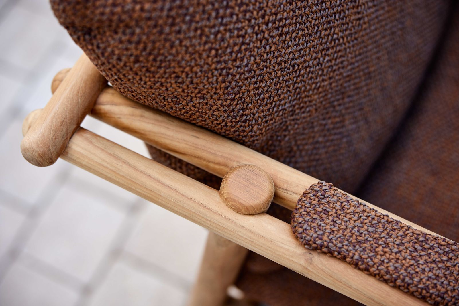 Detailaufnahme des Cane-Line Sticks Loungesessels mit braunem Kissen und Teakholz-Armlehne für den Garten.
