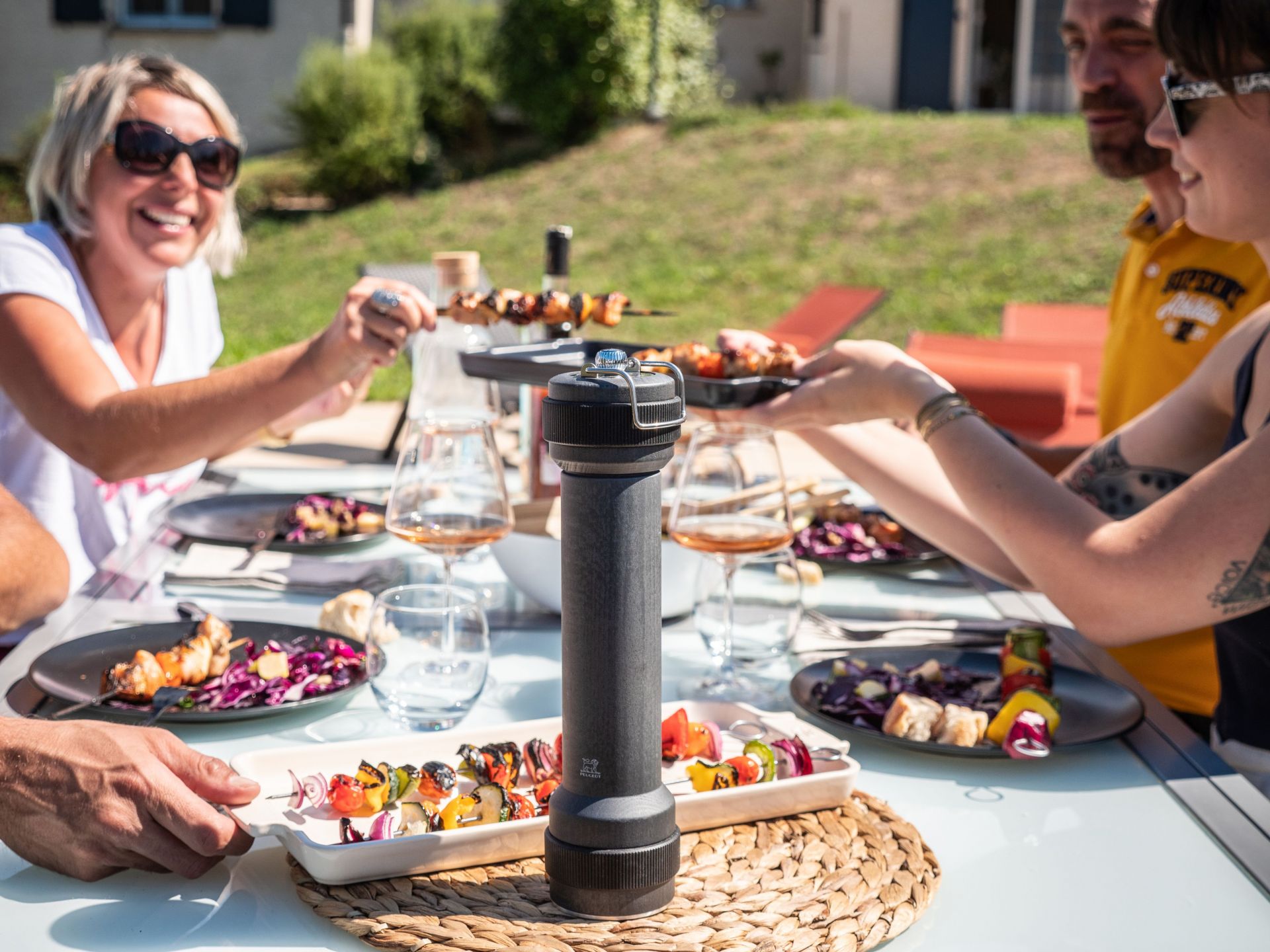 BBQ Szene mit Peugeot Pfeffermühle graphit 30 cm im Fokus, Grillspieße und Salate auf dem Tisch.