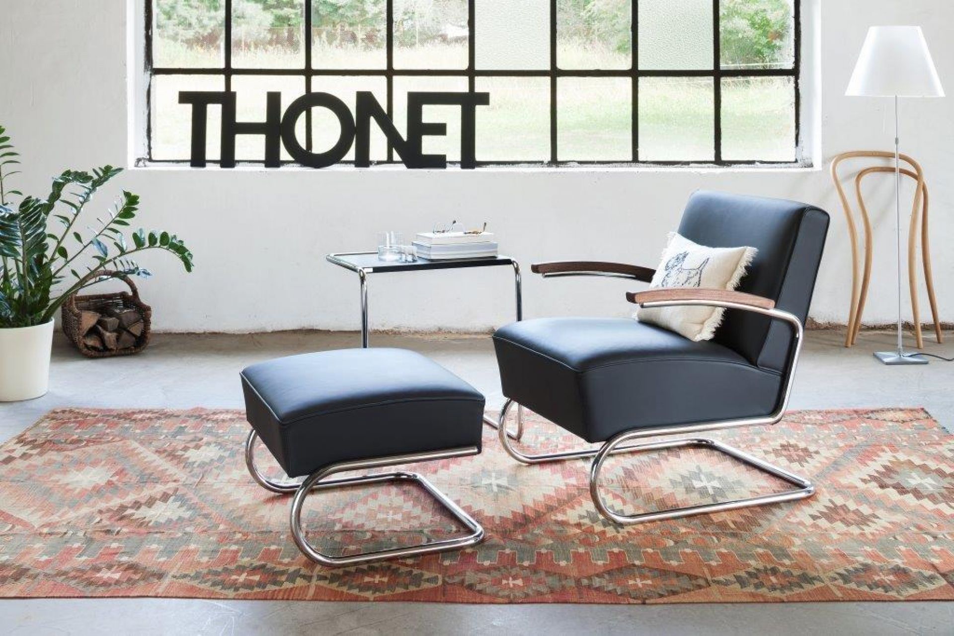 Schwarzer S 411 Thonet Freischwinger Sessel mit Fußhocker und Chromgestell auf gemustertem Teppich.