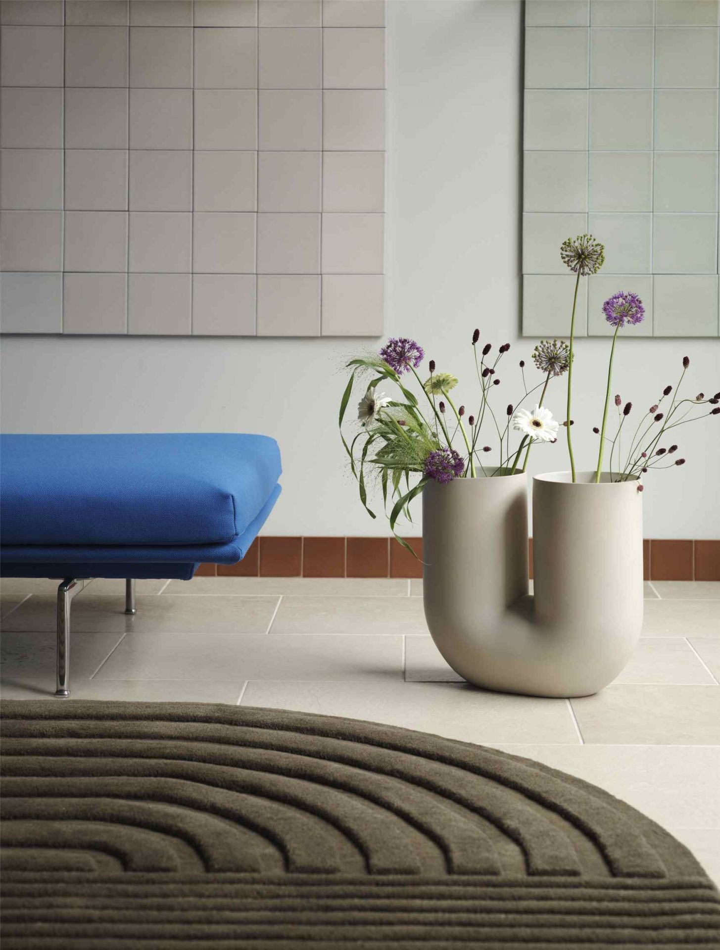 Nahaufnahme der Muuto Kink Vase Sand H 39 cm mit Blumen, stilvolle Wohnzimmerdekoration mit Teppich und Sofa.