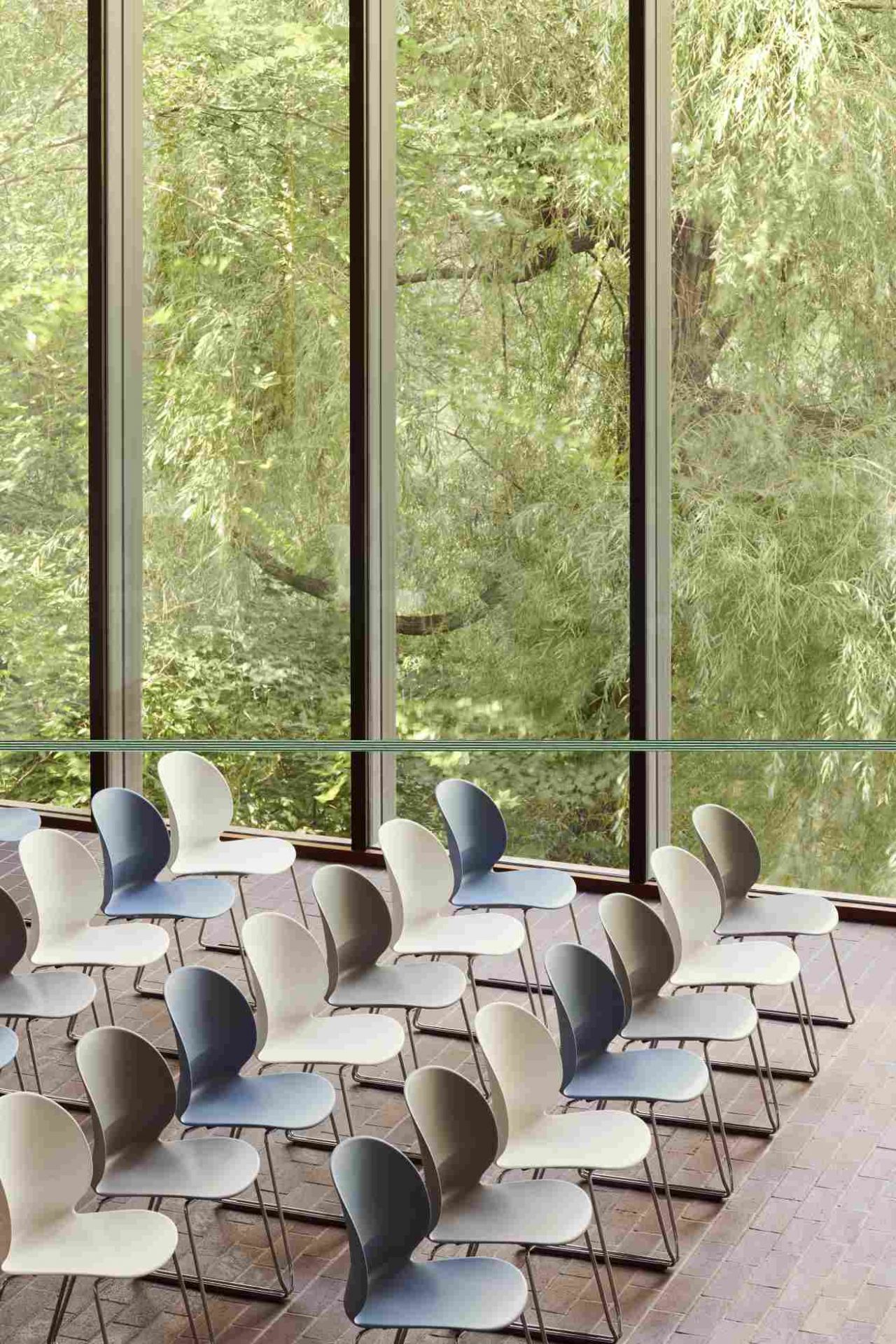 Reihe von Fritz Hansen N02 Recycle Stühlen in verschiedenen Farben vor einem Fenster mit Baumblick.