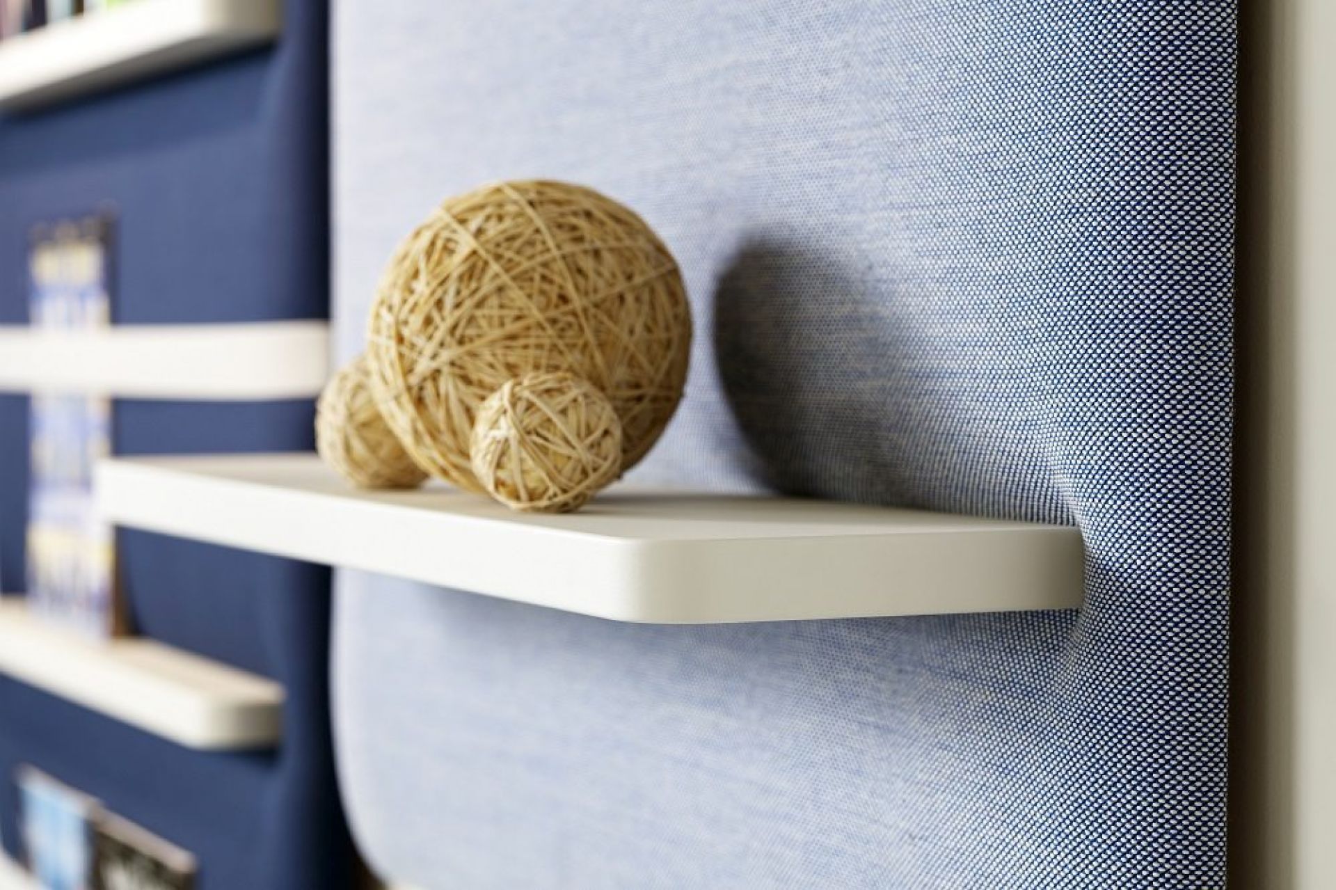 Cascando Pillow Wall Paneel: Detailaufnahme mit Regalboden und Dekoration vor blauem, stoffbezogenem Wandpaneel.
