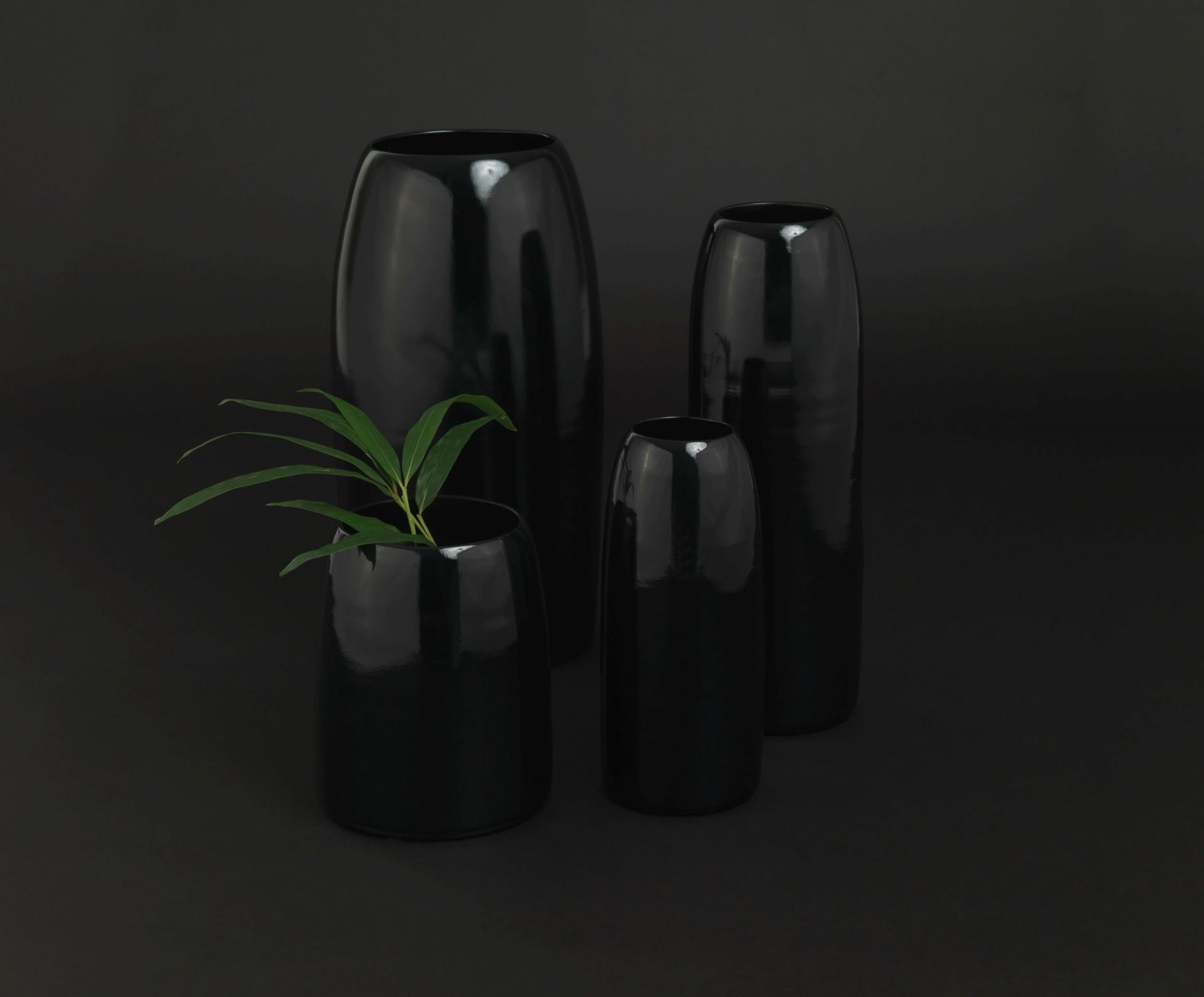 Schönbuch Carla Vase L, ein Set aus vier eleganten, glänzenden, schwarzen Design Vasen auf dunklem Hintergrund.