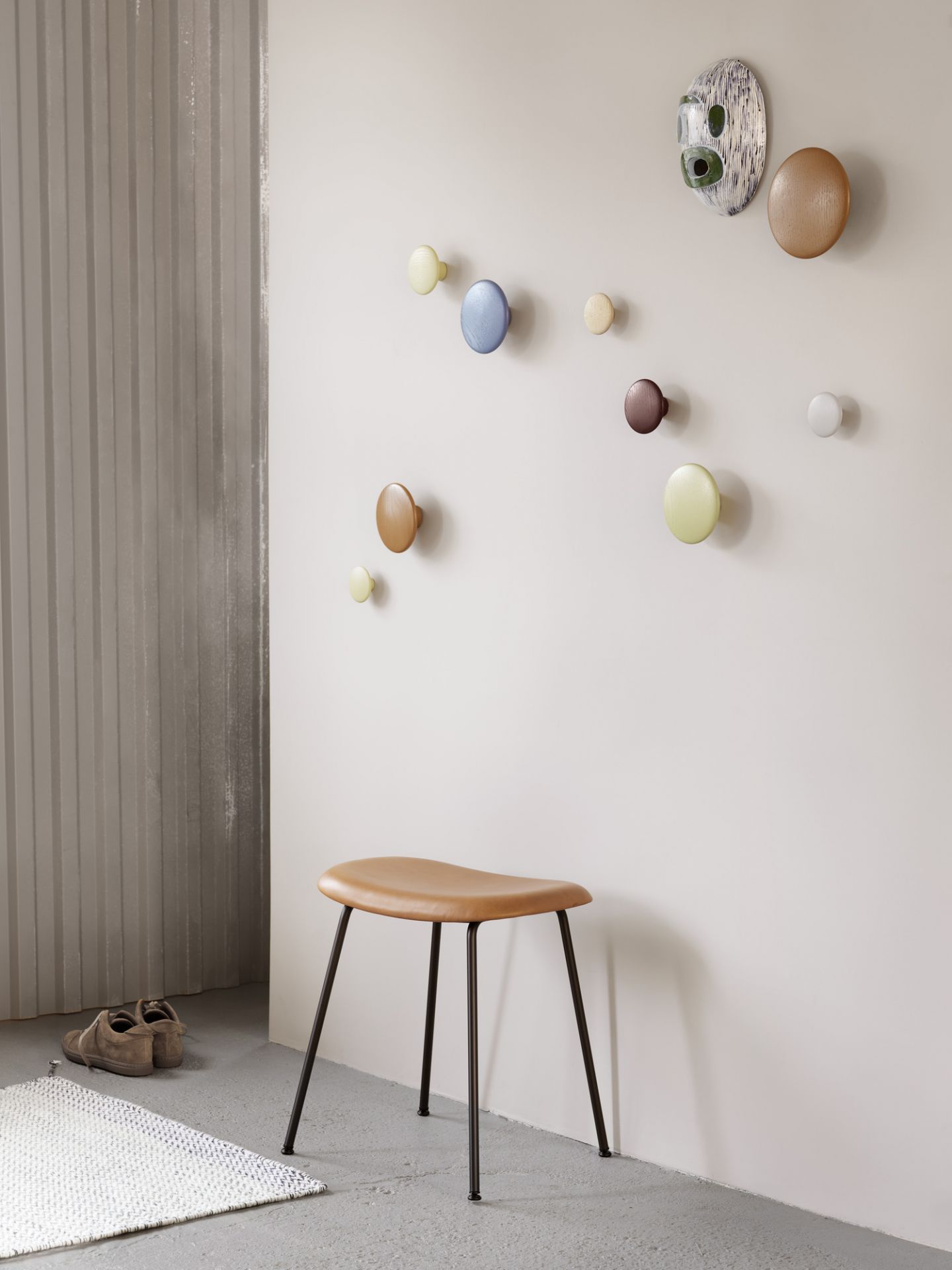 Muuto Fiber Stool Hocker mit brauner Sitzfläche und schwarzen Beinen vor Wand mit Garderobenhaken.