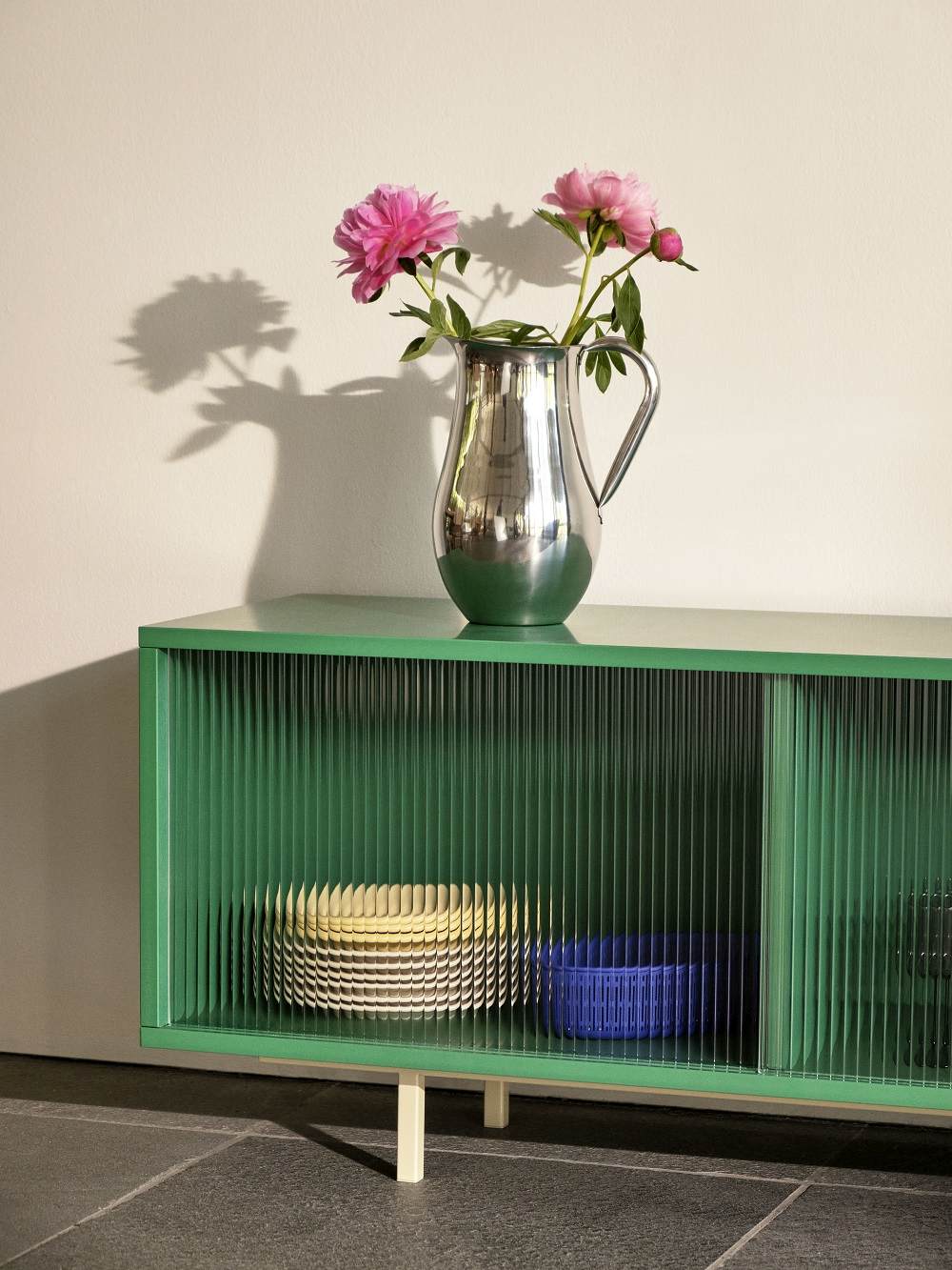 Mintfarbenes Hay Sideboard mit Glasfront, Geschirr im Inneren und Blumenvase auf der Ablage.