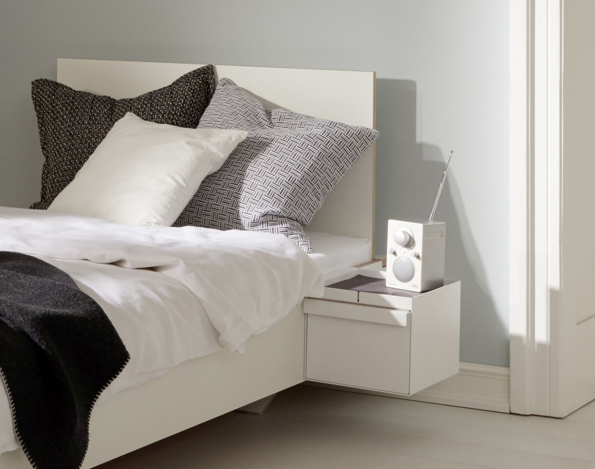Weißes Flai Einzelbett von Müller Möbelwerkstätten mit Nachttisch und Radio im Schlafzimmer.