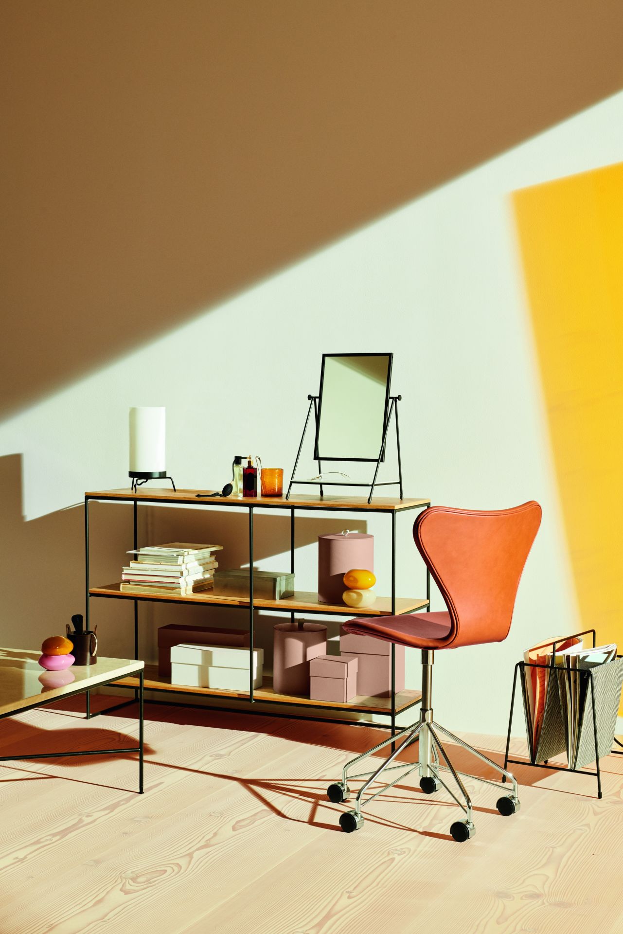 Orangefarbener Siebener Drehstuhl von Fritz Hansen vor Regal und gelber Wand. Design Bürostuhl.