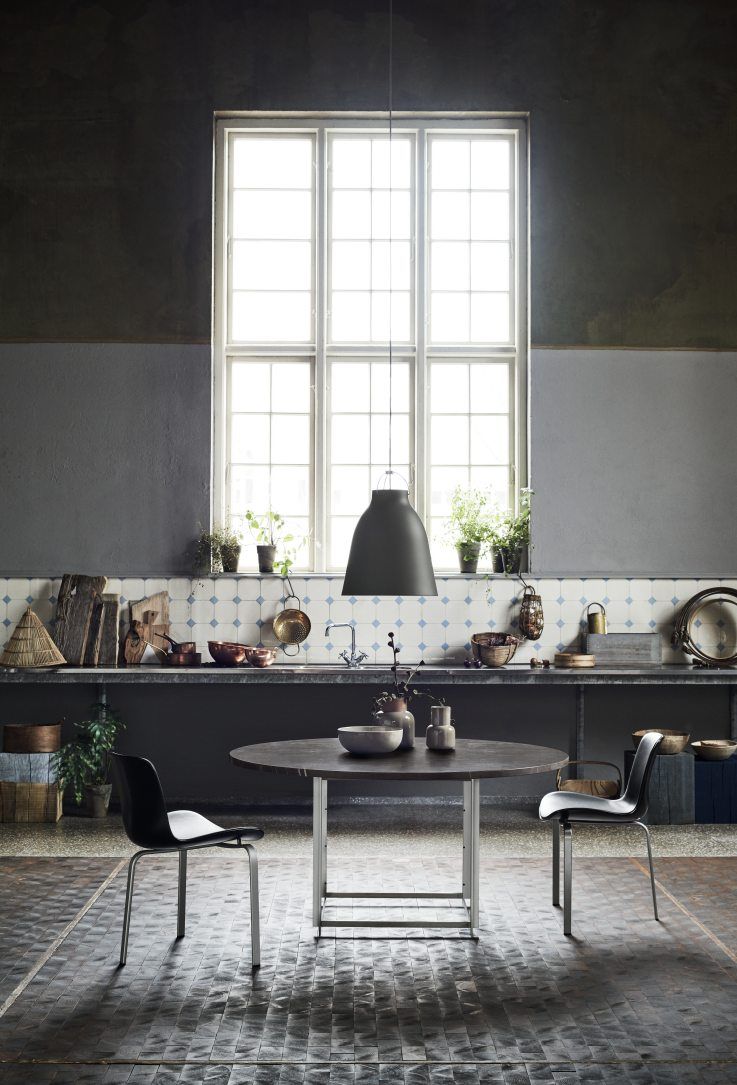 Graue Caravaggio Pendelleuchte von Fritz Hansen über Esstisch in stilvollem Interieur mit Küchenelementen.