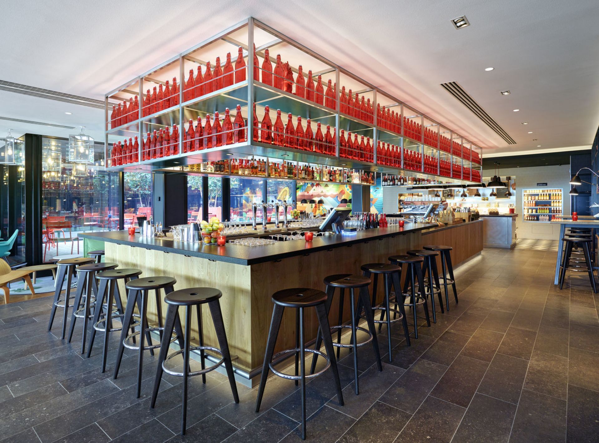 Innenaufnahme einer Bar mit Vitra Tabouret Haut Barhockern aus dunklem Holz und Metallfußstütze vor Bartresen.
