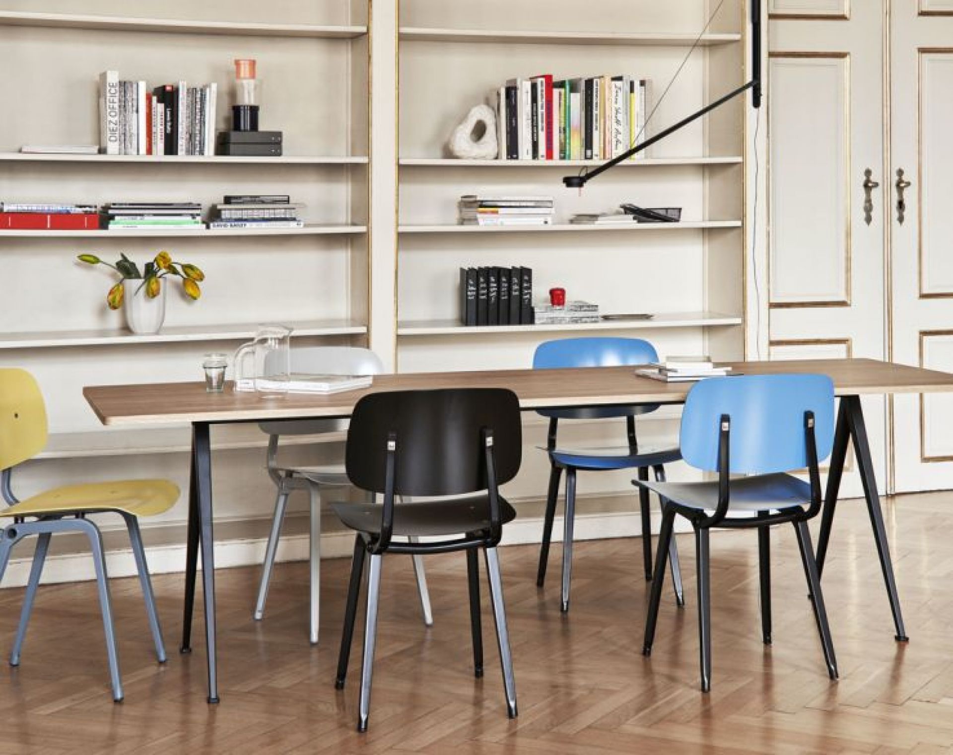 Esstisch mit mehreren Revolt Chair Stühlen von Hay in verschiedenen Farben vor einem Bücherregal.