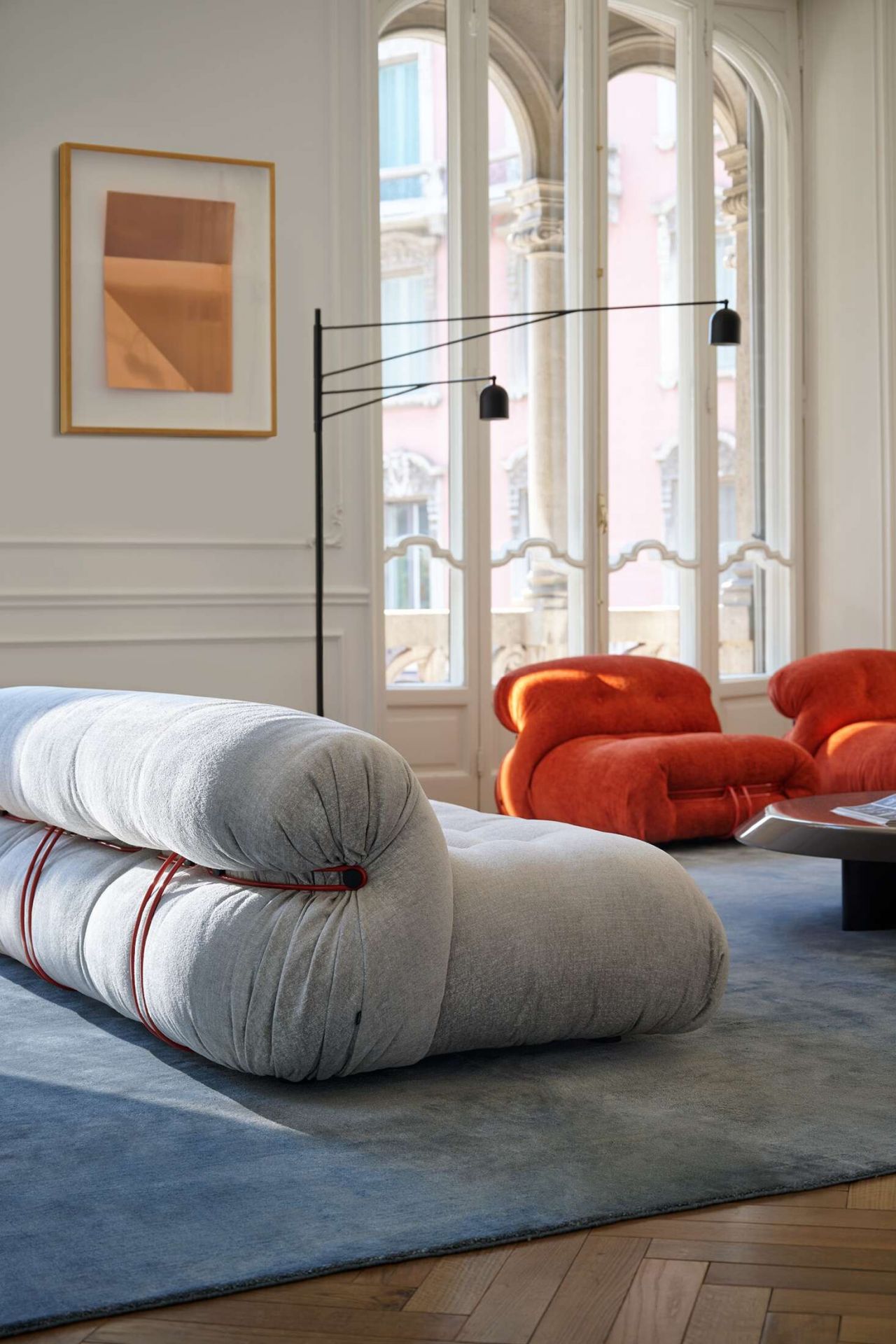 Helles Wohnzimmer mit Cassina Soriana Sofa in Grau, roten Akzenten und orangefarbenen Sesseln.