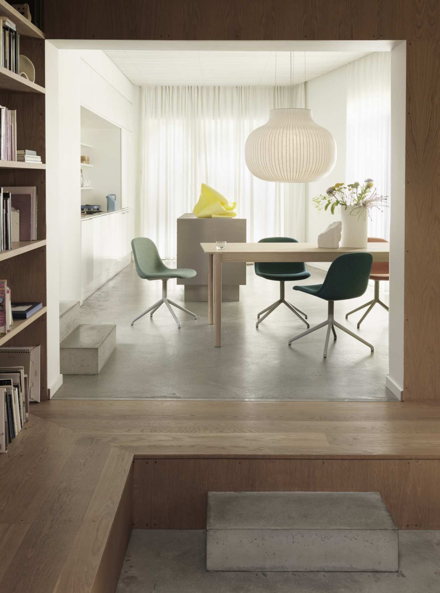 Helle skandinavische Esszimmer-Szene mit Muuto Strand Pendelleuchte, Esstisch und grünen Stühlen unter sanftem Licht.