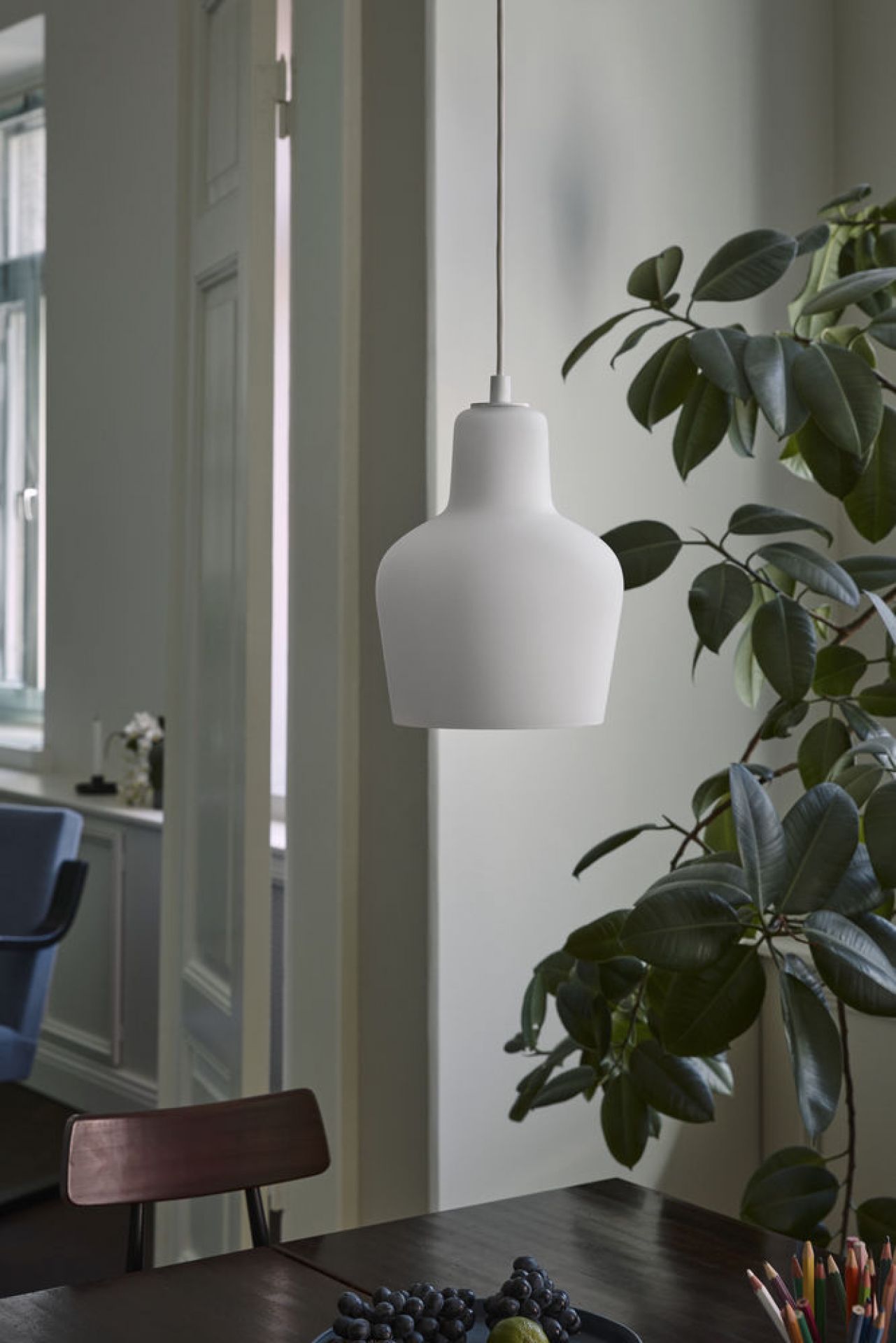 Weiße Artek A440 Hängeleuchte über Esstisch mit Obst und Zimmerpflanze im modernen Interieur.