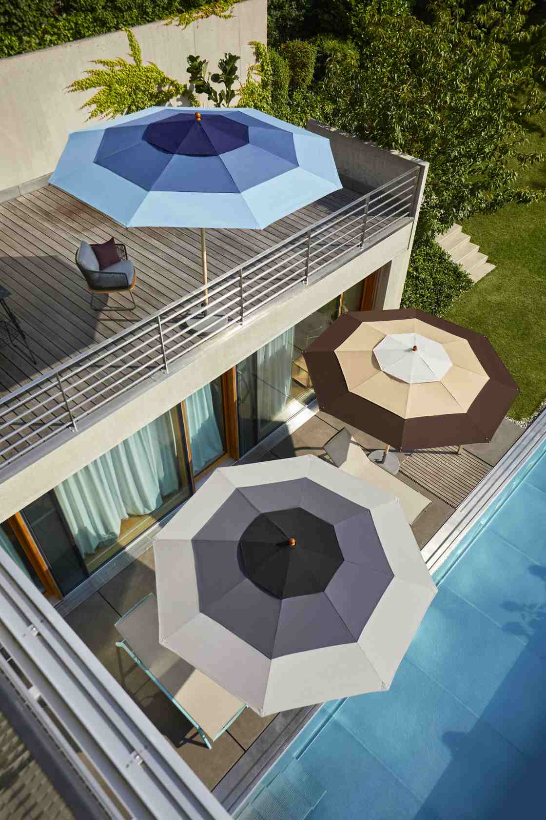 Draufsicht von drei farbigen Weishäupl Sonnenschirmen, die auf einer Terrasse mit Pool für Schatten sorgen.