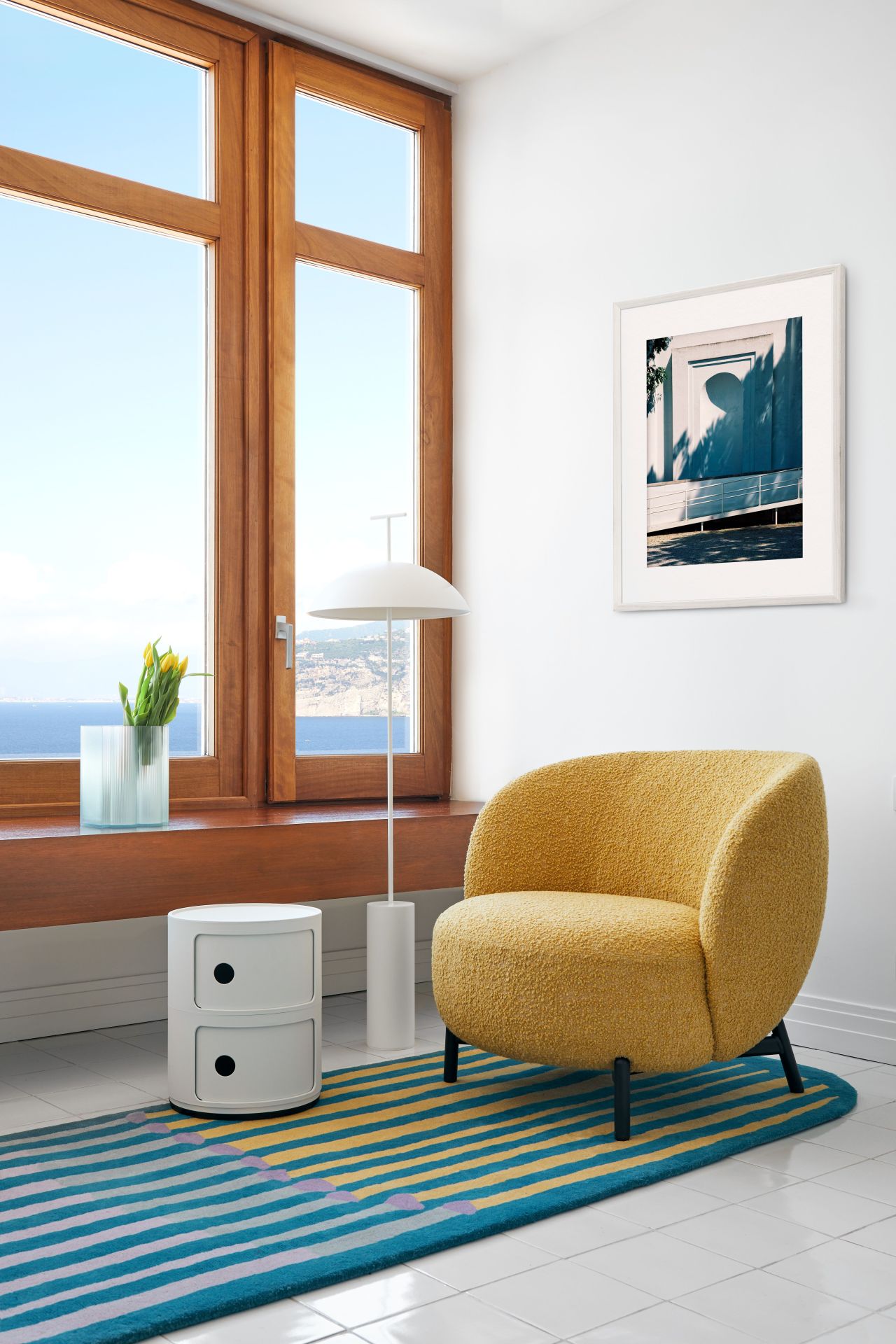 Weißes Componibili 2er Element von Kartell neben gelbem Sessel und Fenster mit Meerblick.