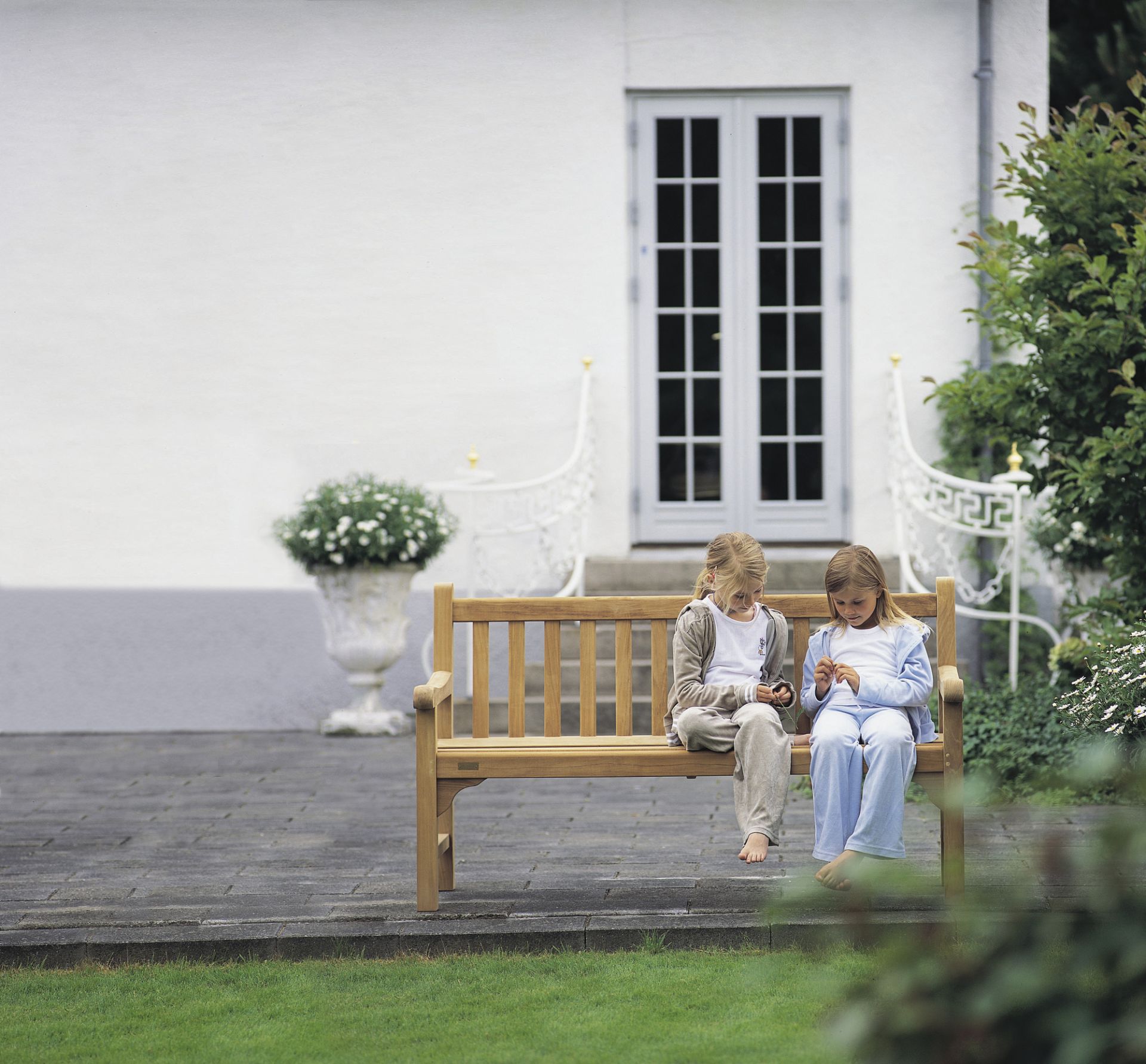 Zwei Mädchen sitzen auf der England Bank von Skagerak im Garten. Outdoor Gartenbank.