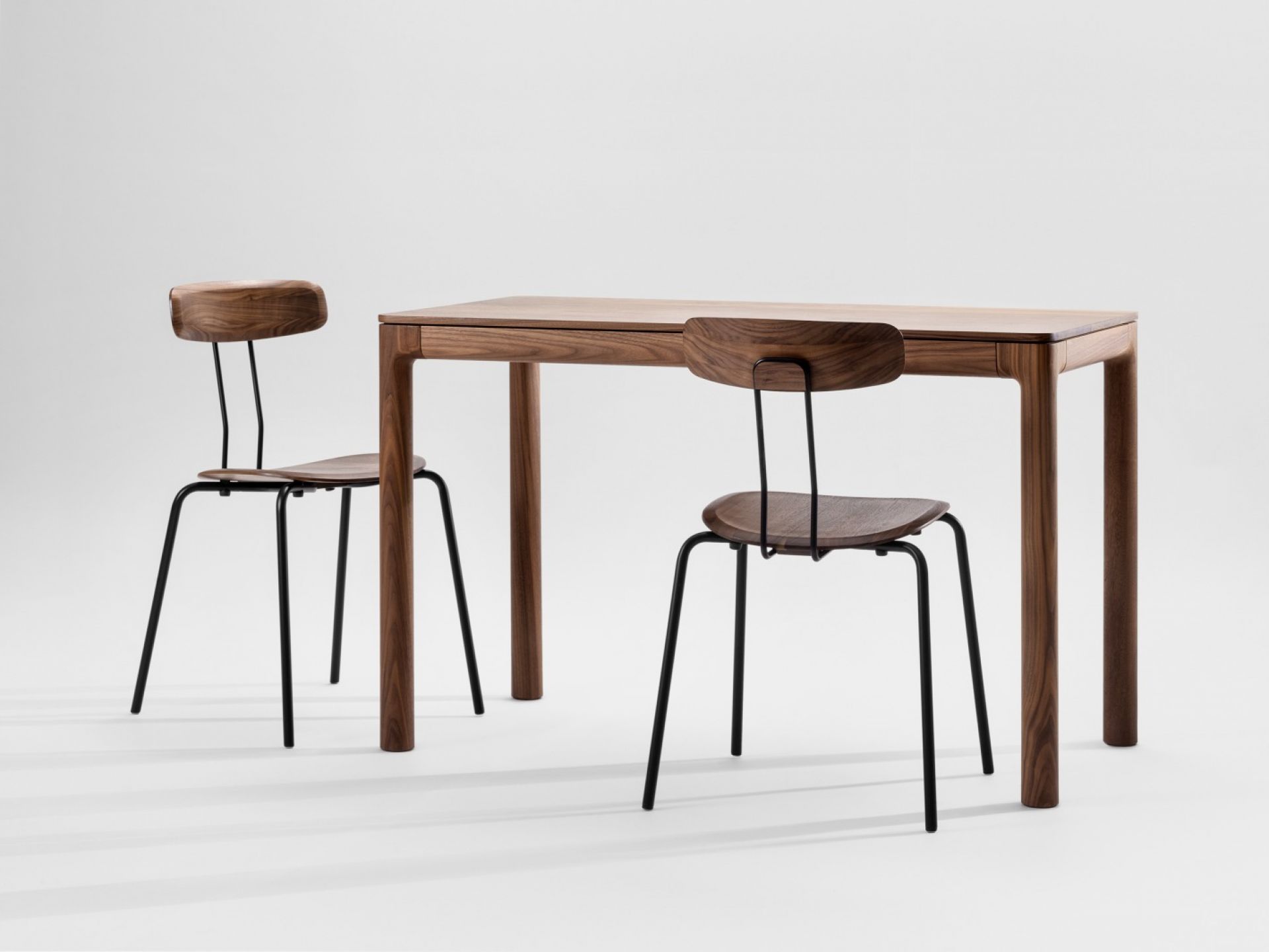Okito Chair Stuhl und Esstisch aus Holz mit schwarzen Metallbeinen vor neutralem Hintergrund.