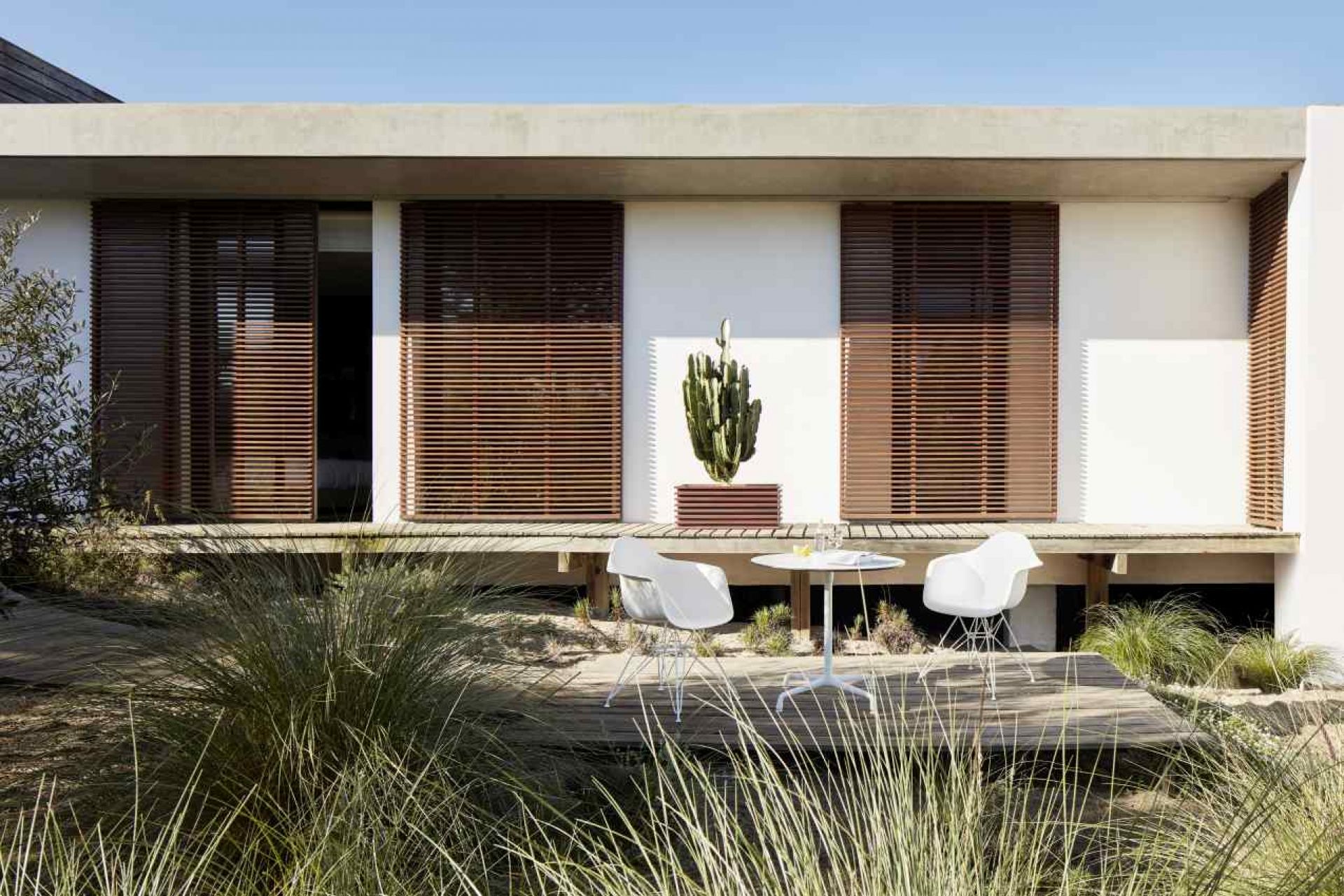 Eames Contract Table von Vitra, runder Tisch mit weißen Stühlen auf einer Holzterrasse vor modernem Haus.