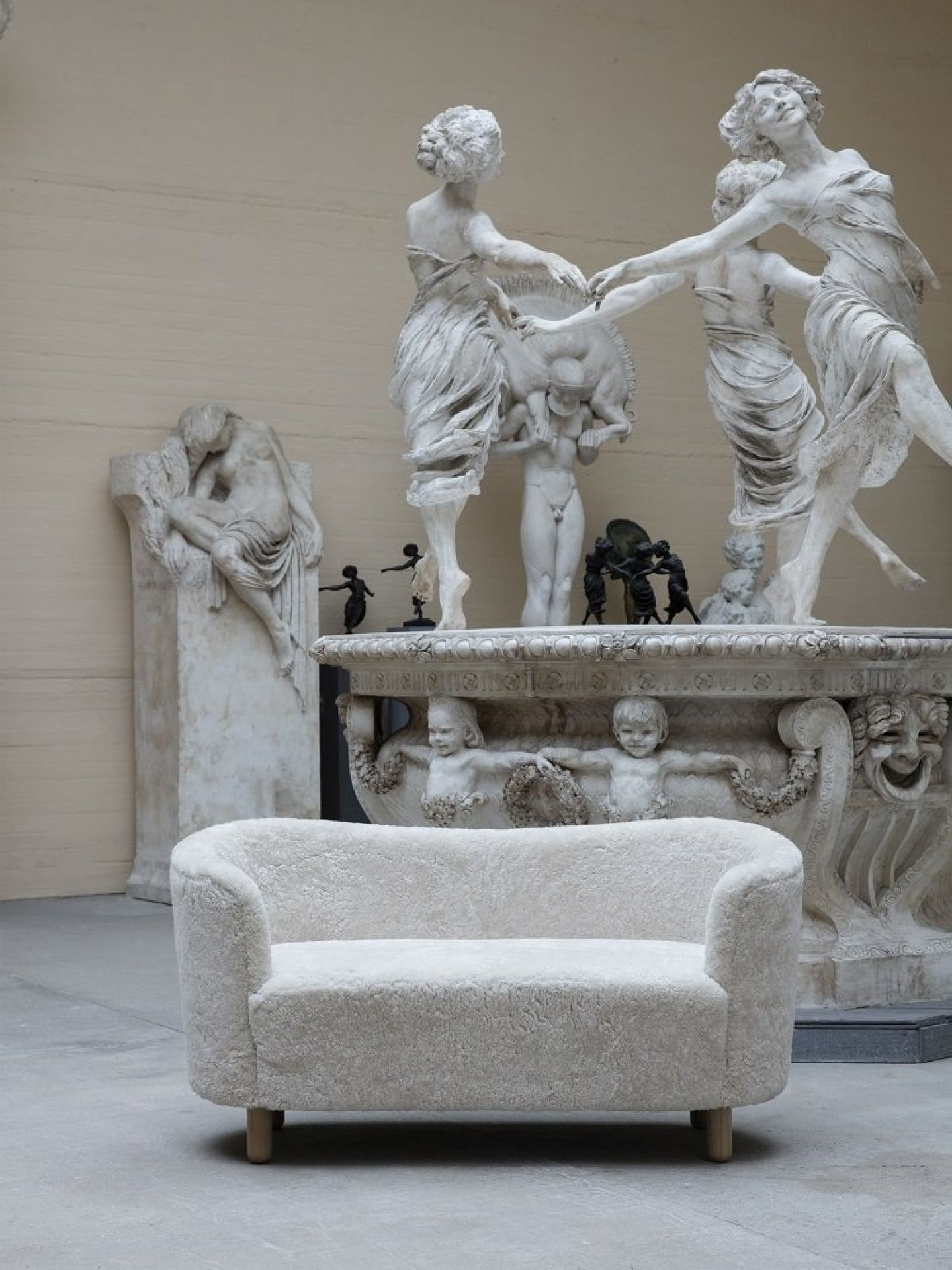 Audo Mingle Sofa, ein cremefarbenes 2-Sitzer Sofa aus Stoff, vor Statuen in einem Museum.