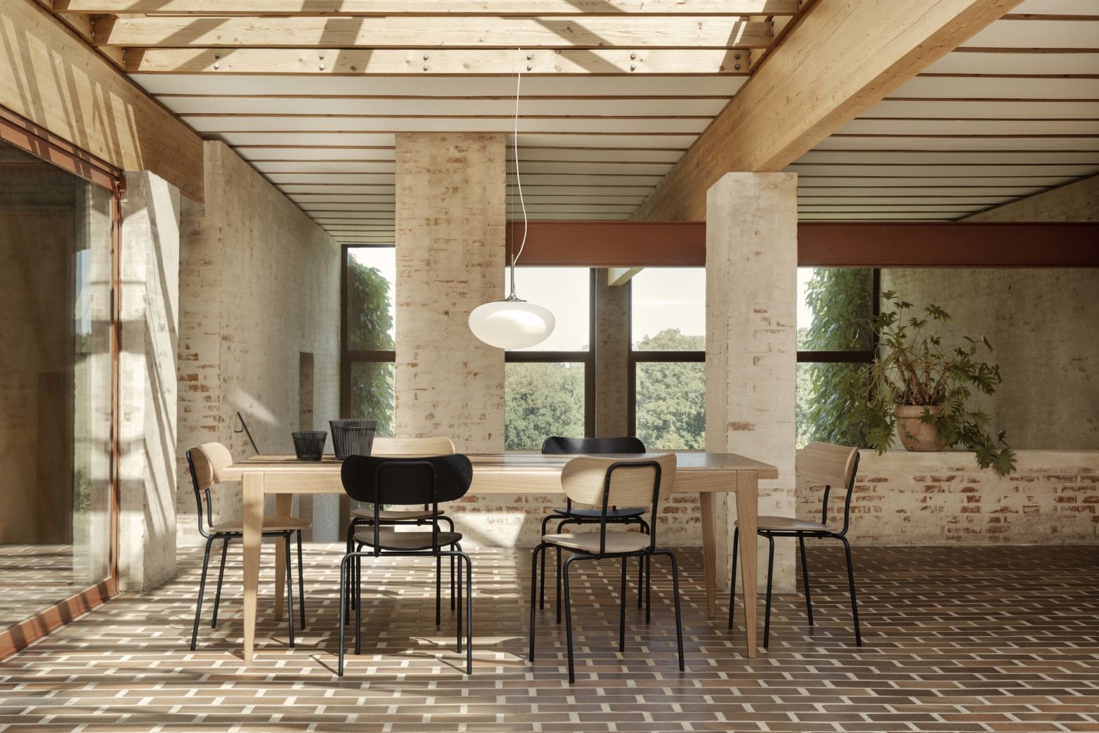 Esszimmer mit Gubi S-Table Esstisch aus hellem Holz und Stühlen auf einem Ziegelboden.