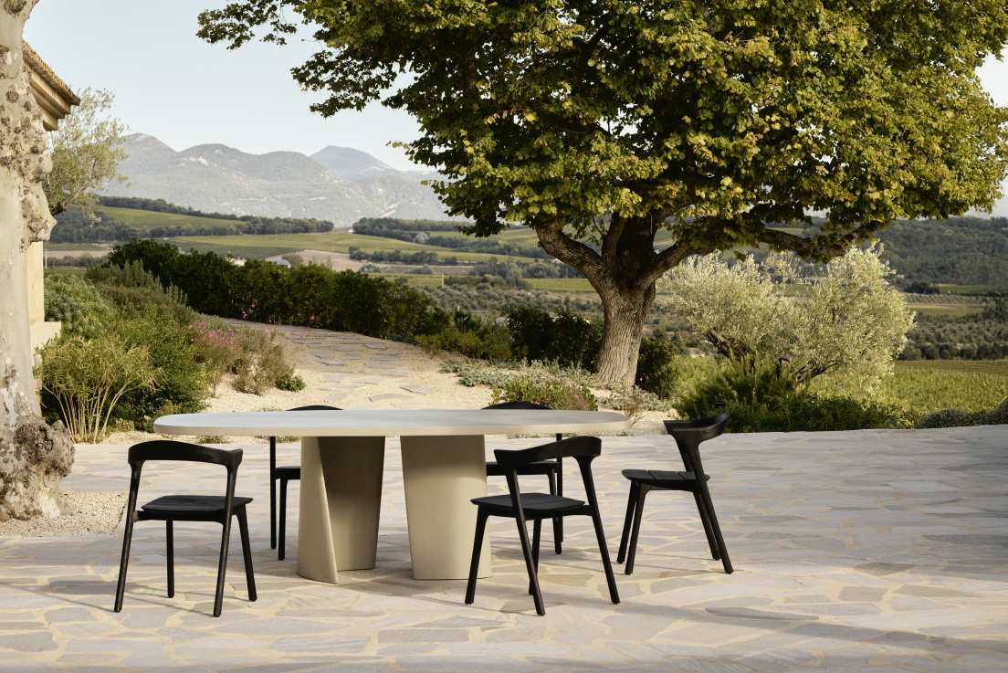 Canyon Outdoor Esstisch von Ethnicraft aus Beton mit schwarzen Stühlen im Garten.
