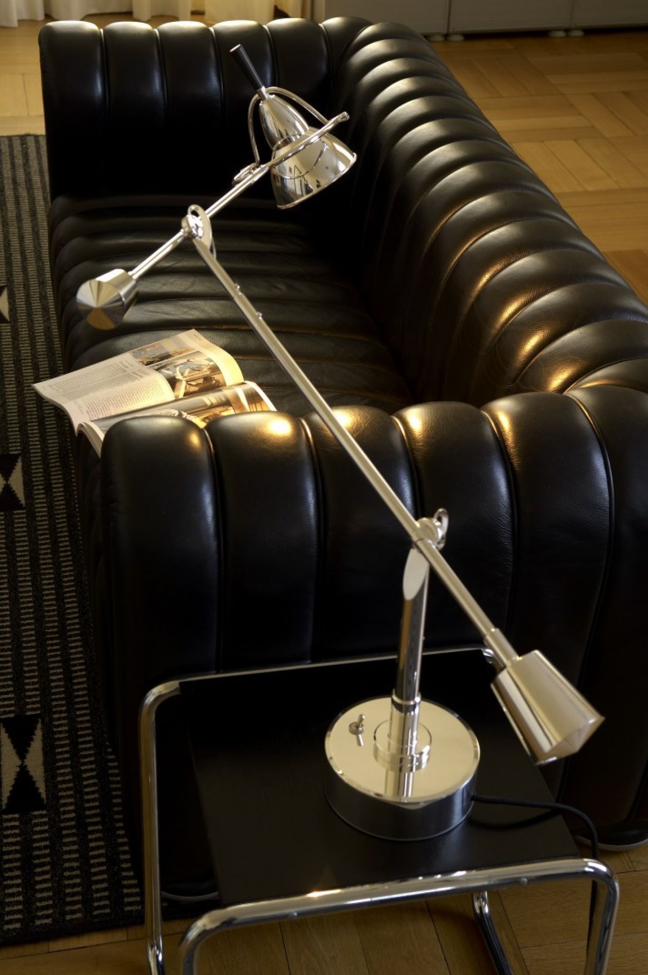 Verstellbare Chrom Schreibtischlampe auf schwarzem Beistelltisch neben Ledersofa, modernes Wohnzimmer Interieur.