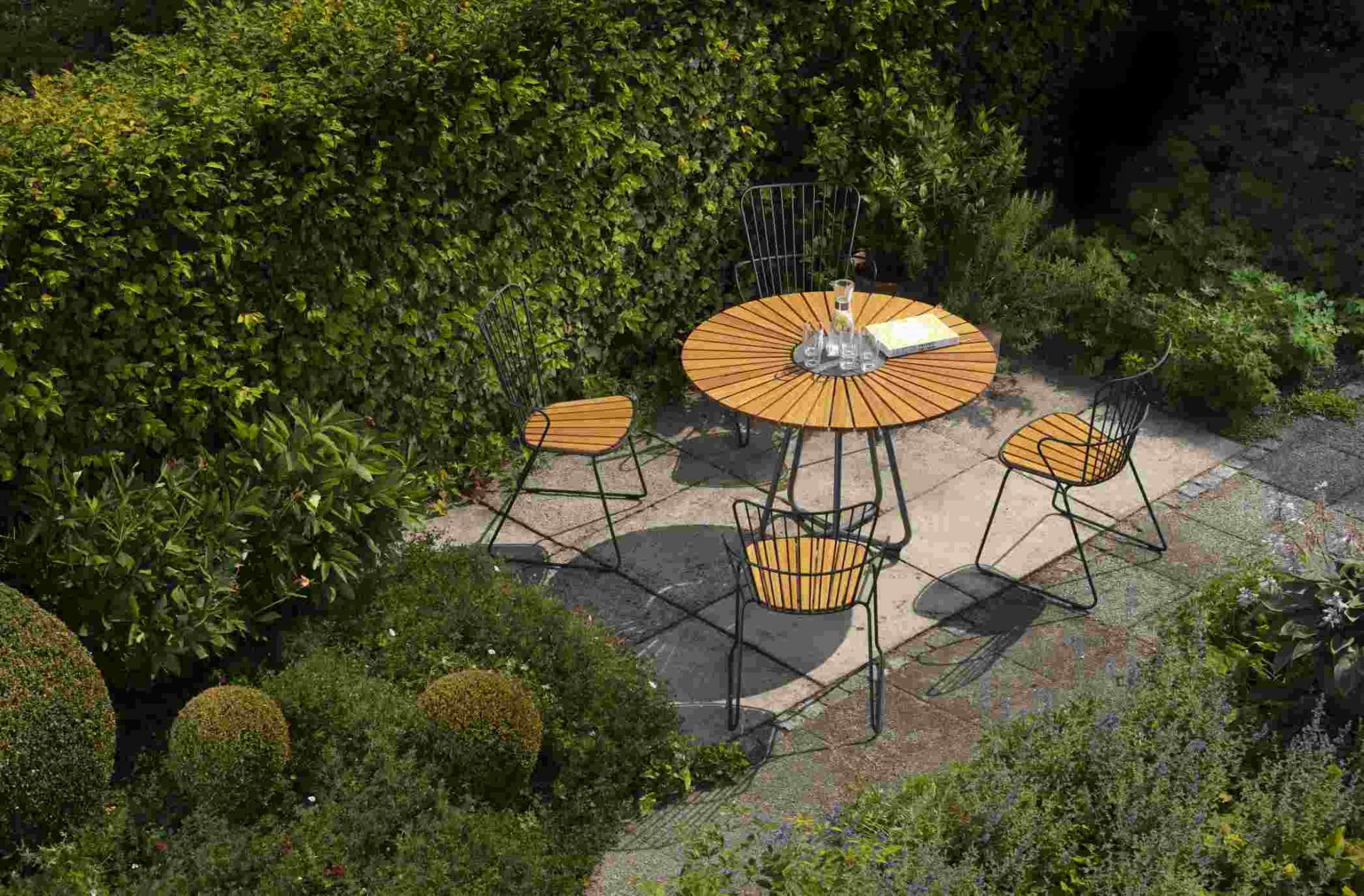 Houe Circle Gartentisch Ø 110 cm mit vier Stühlen auf einer Terrasse im Grünen.